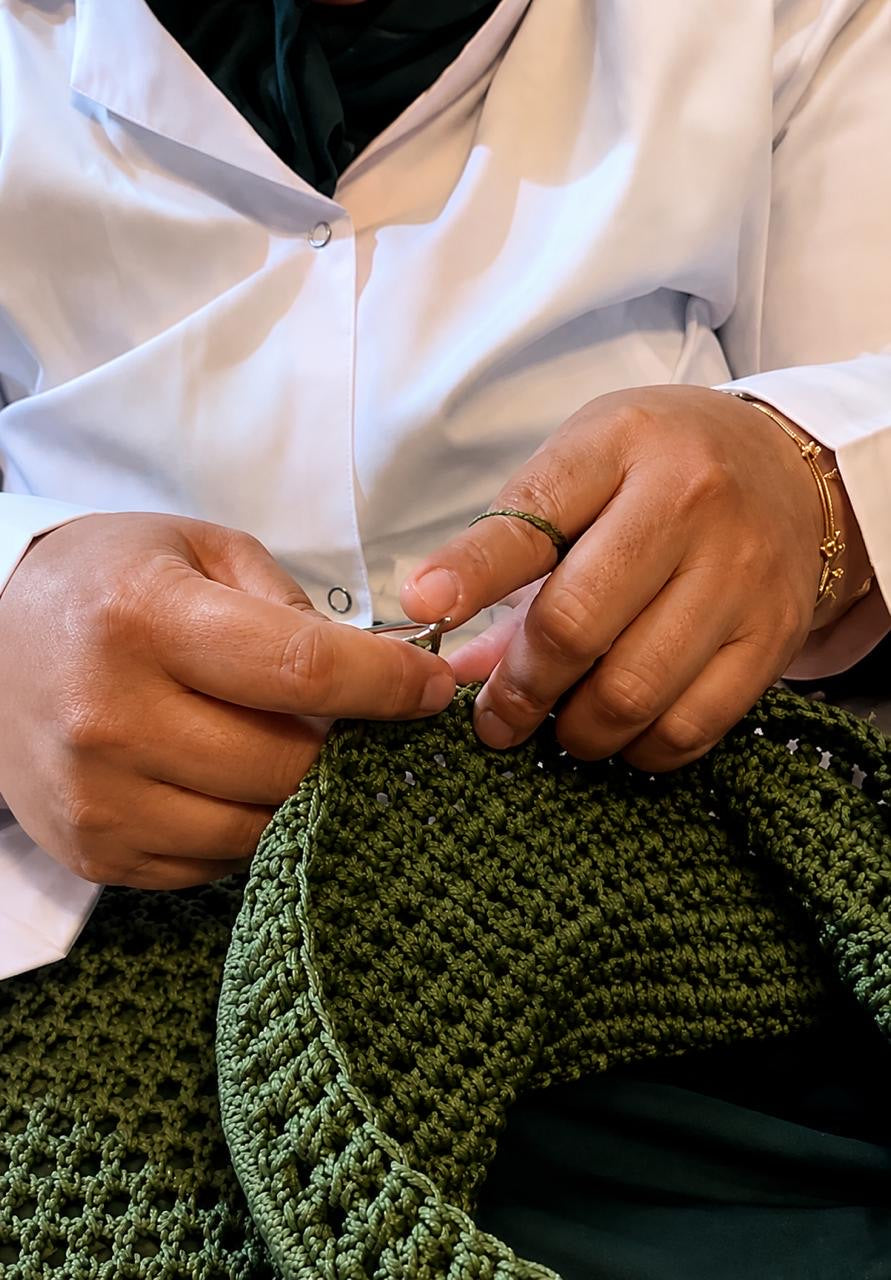Hands using a crochet hook to work textured green yarn in the Maison Azzar workshop