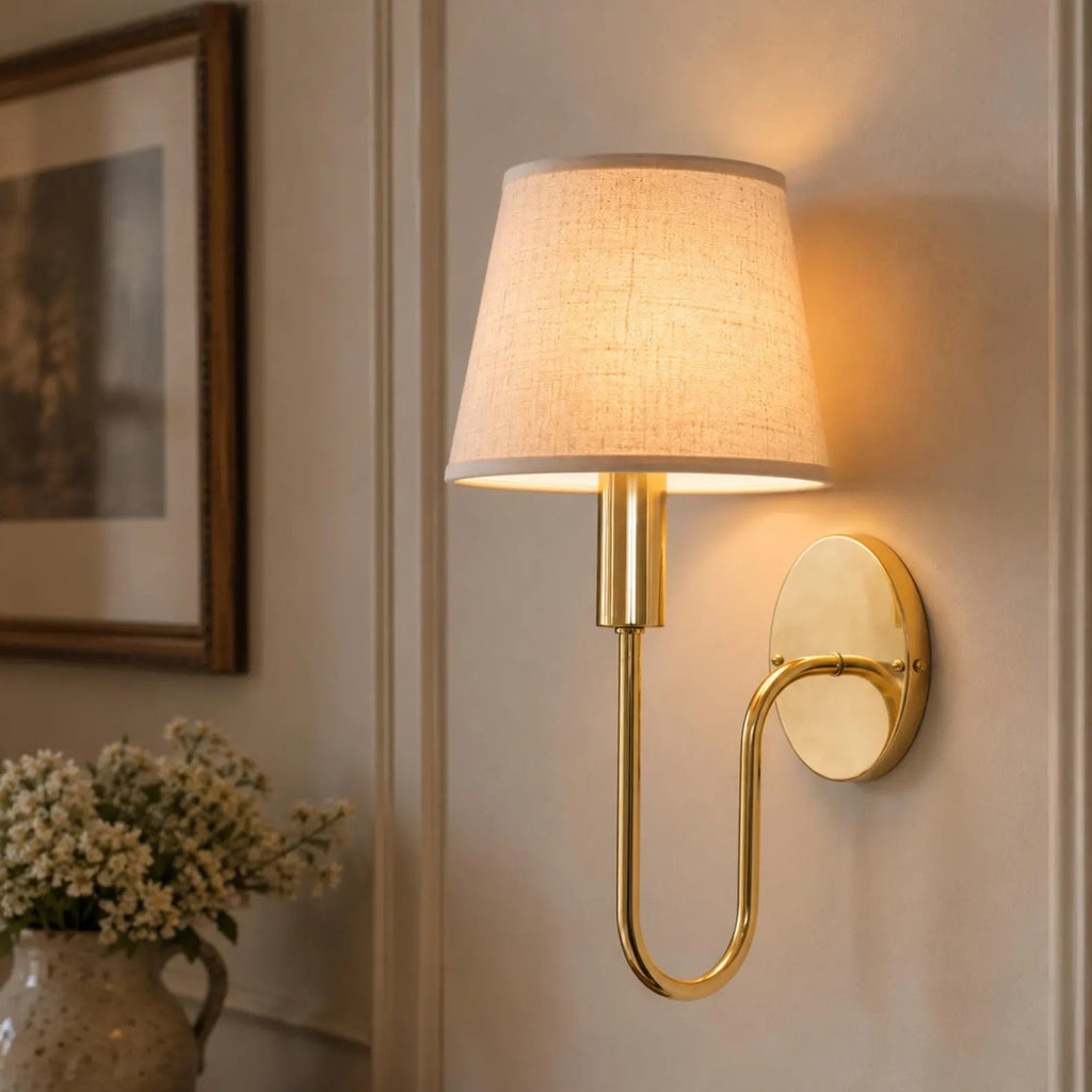 Brass wall sconce with the optional linen shade illuminated in an interior