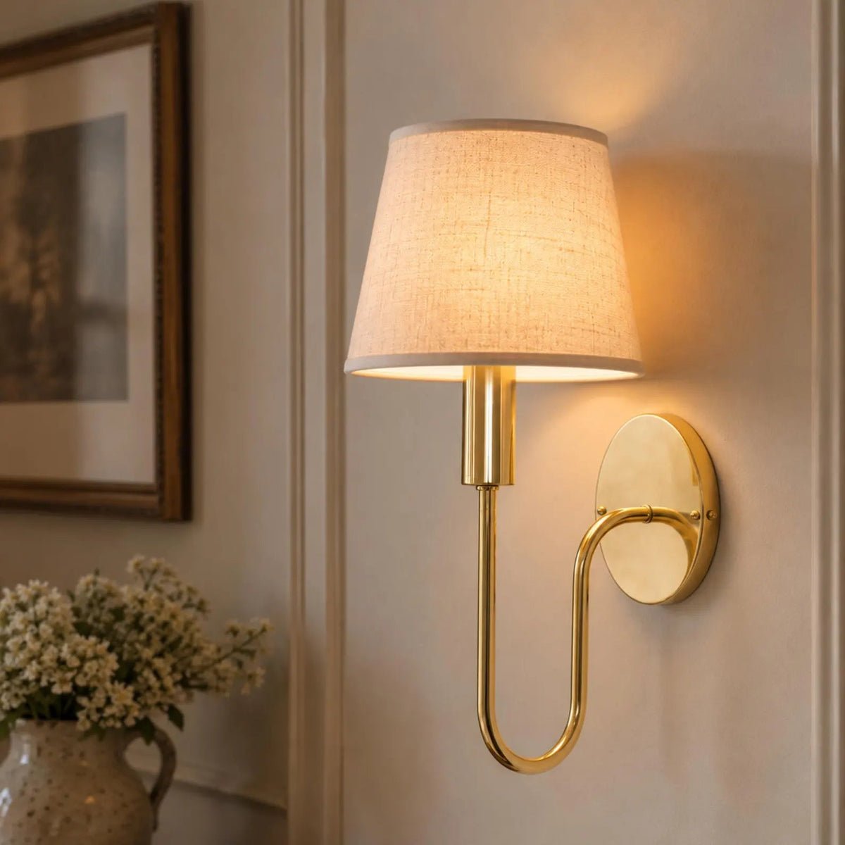 Brass wall sconce with the optional linen shade illuminated in an interior