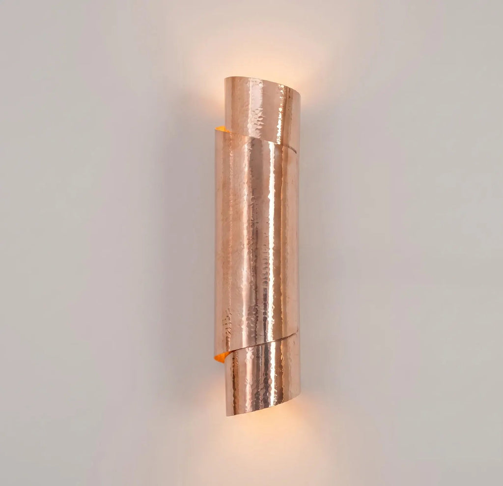Illuminated sculptural hammered copper wall sconce casting light upward