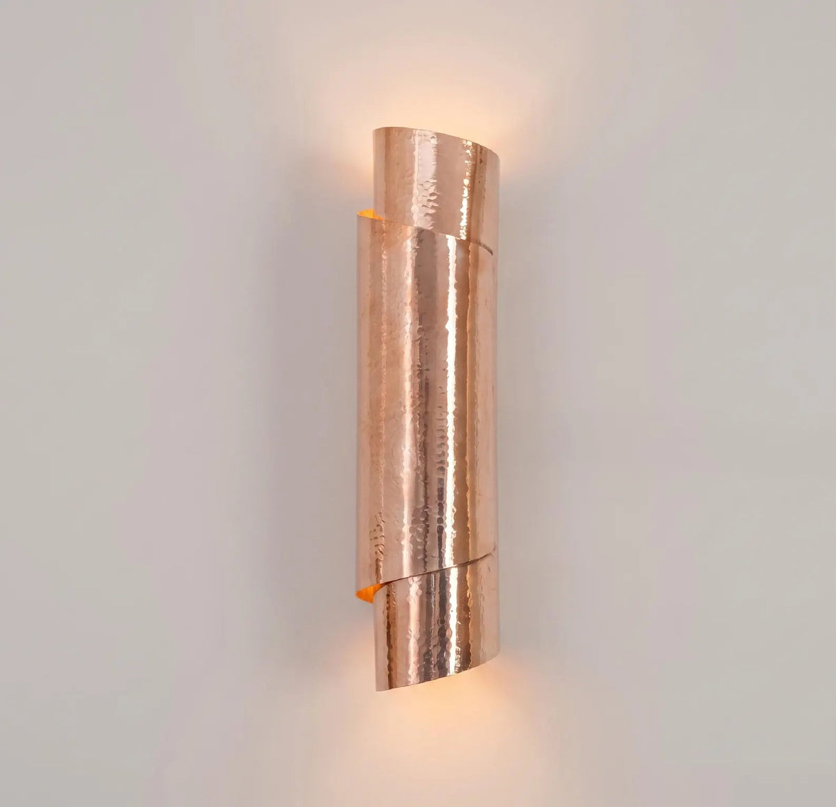 Illuminated sculptural hammered copper wall sconce casting light upward