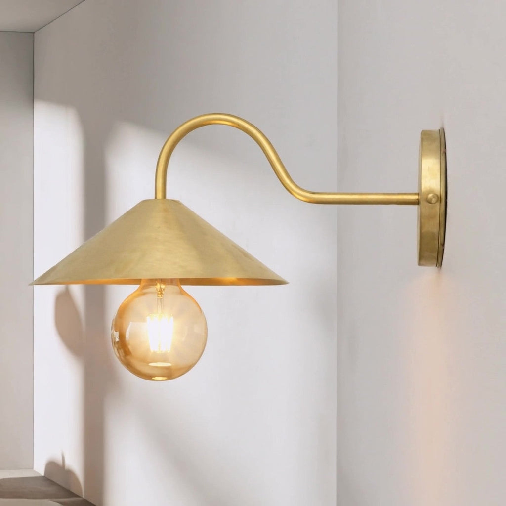 Brass gooseneck wall sconce with conical shade in an interior