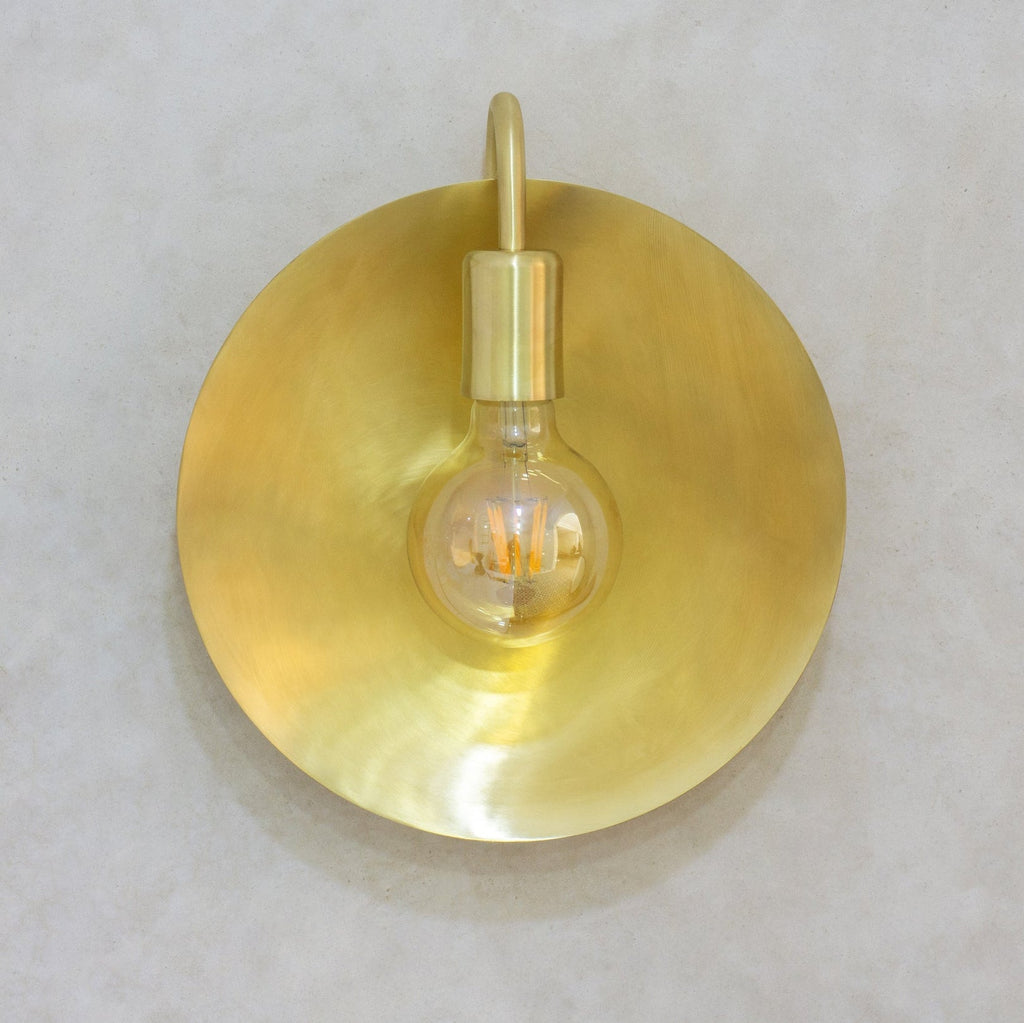 Front view of the circular brushed brass wall sconce