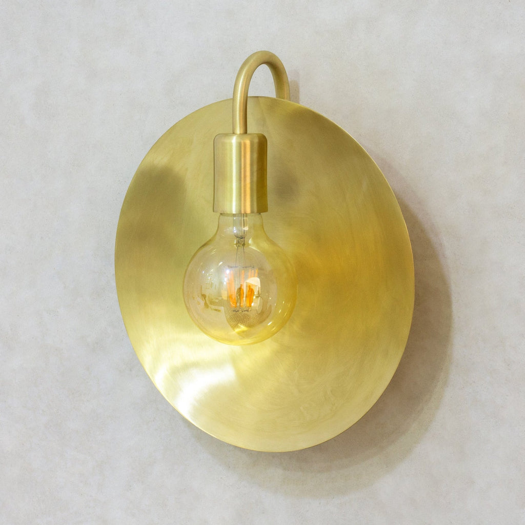 Brushed brass wall sconce showing the round reflector and curved arm
