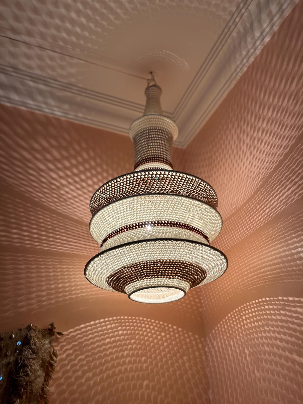 A tiered pendant light fixture featuring a woven, lattice-like structure with alternating bands of cream and dark brown.…