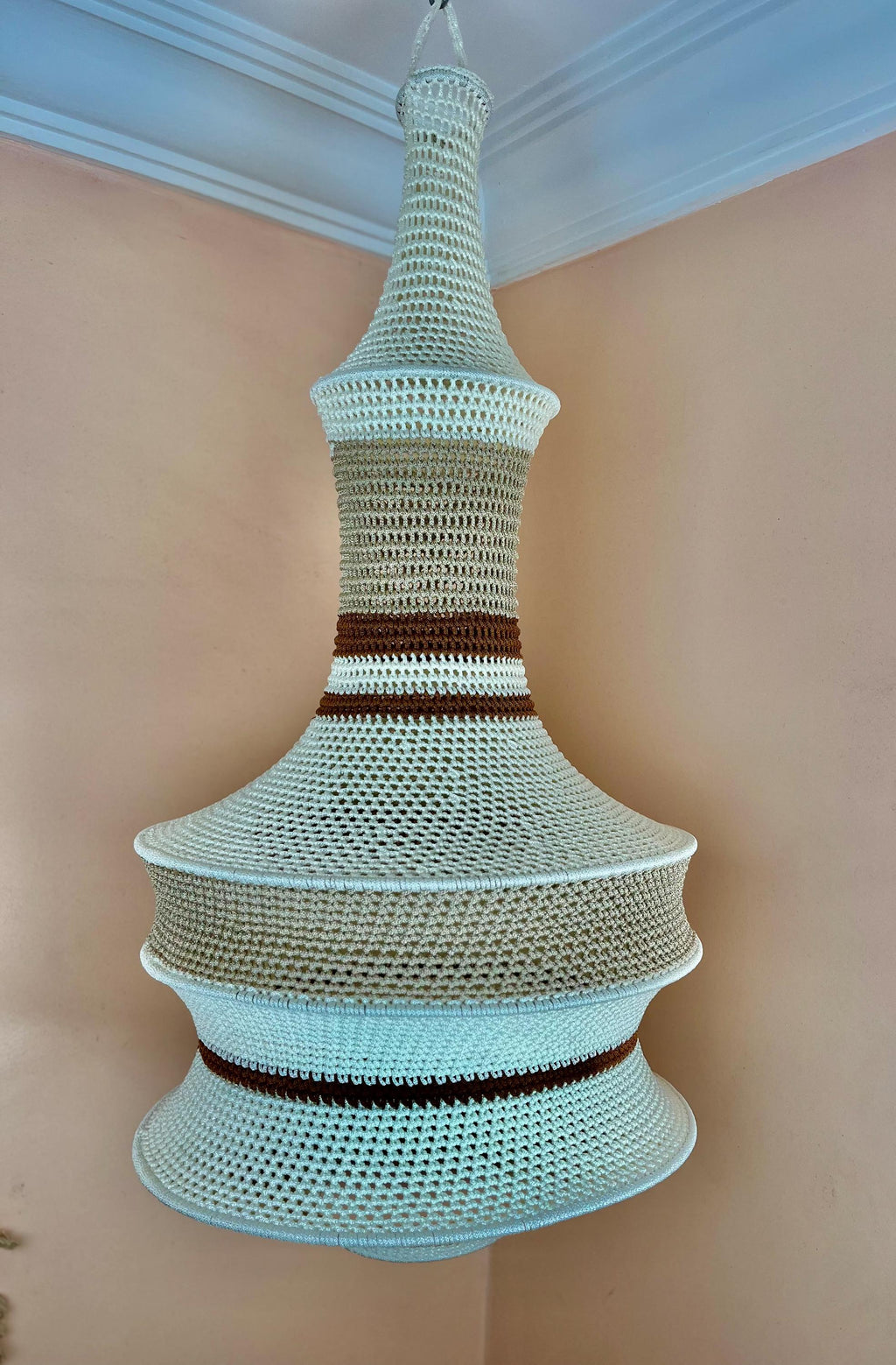 A hanging pendant light shade featuring a multi-tiered, bell-shaped structure crafted from crocheted yarn. The design…