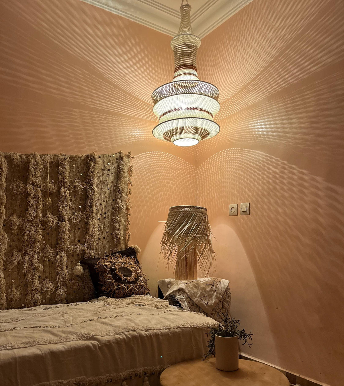 A tiered woven pendant light fixture with a cylindrical top and wide circular shades, emitting a warm glow that casts…