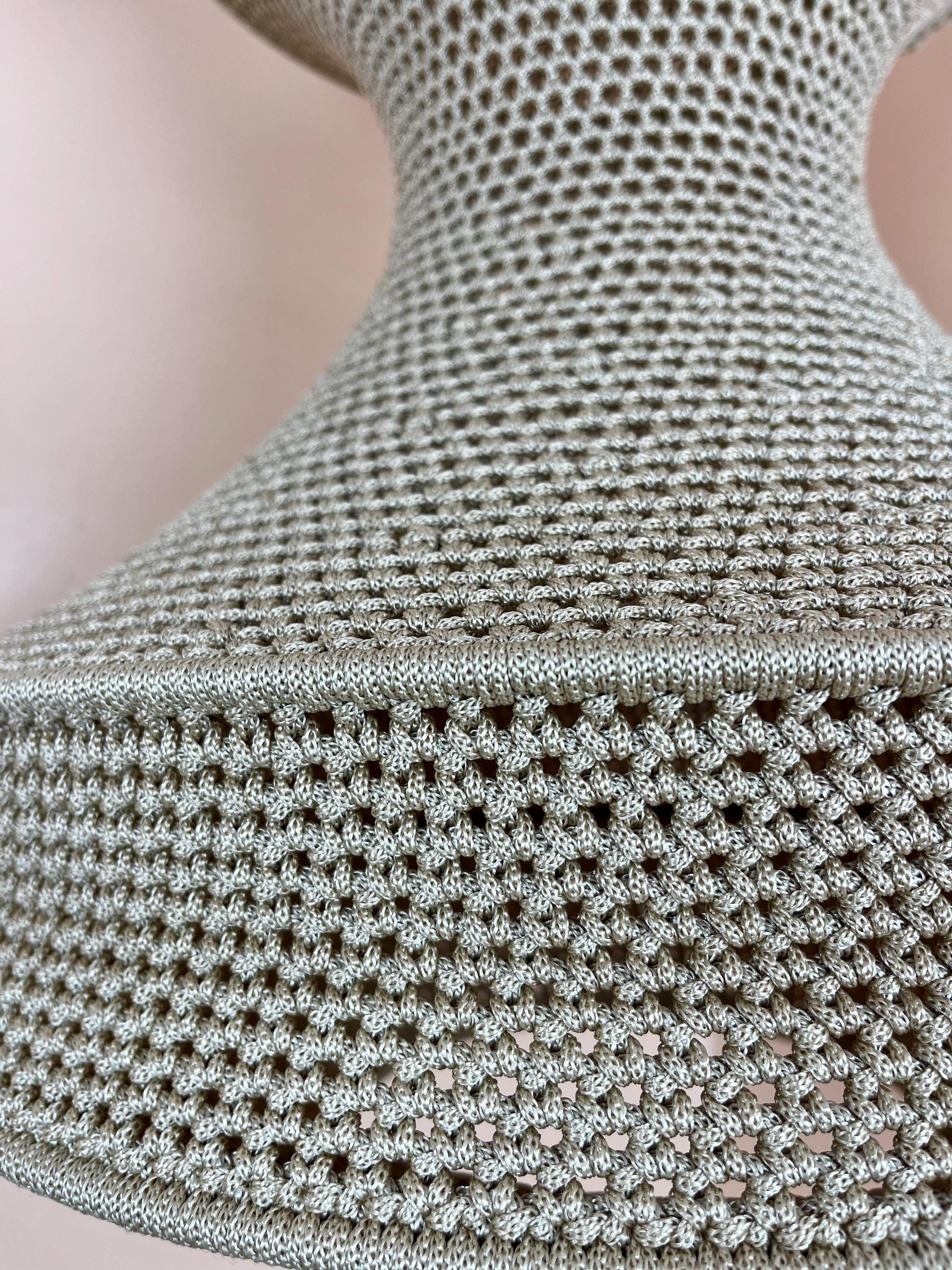 A beige lampshade featuring a dense, intricate crochet knit pattern with a visible horizontal seam separating the upper…