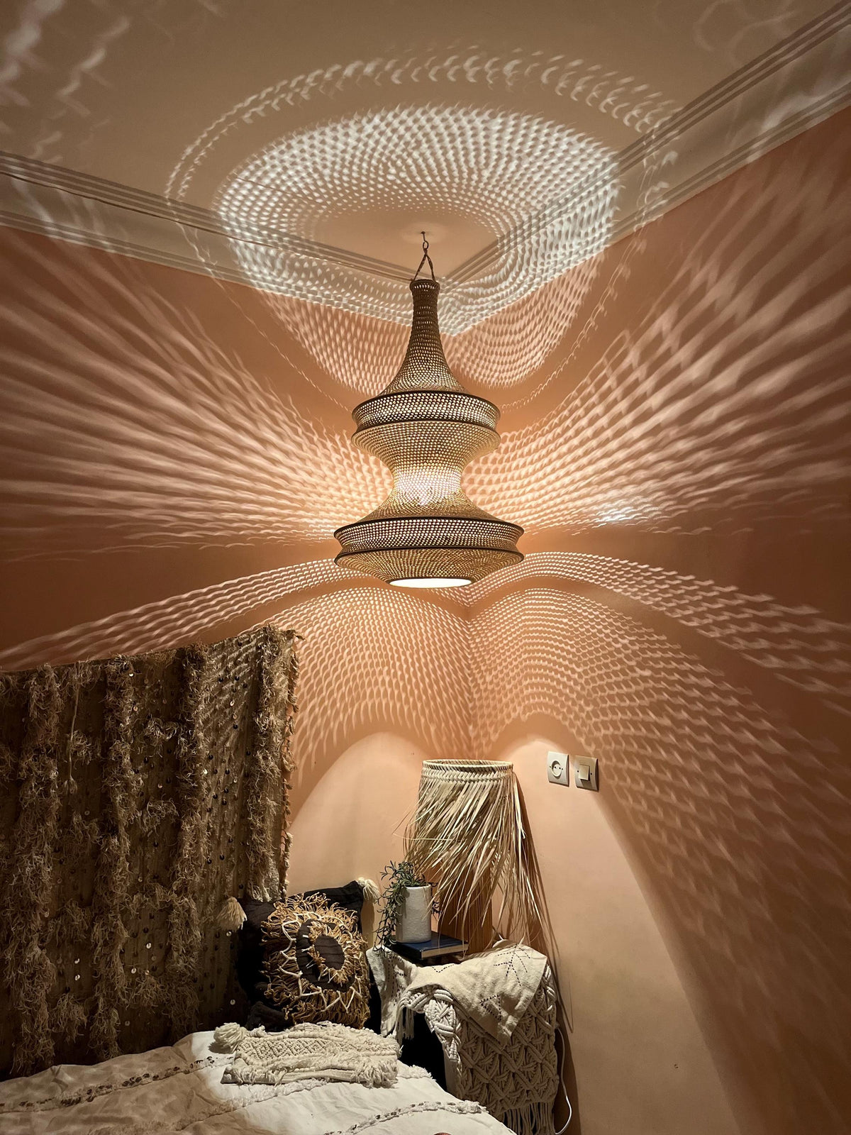 A woven pendant light fixture with a tiered, hourglass-shaped silhouette hangs from the ceiling, casting intricate,…