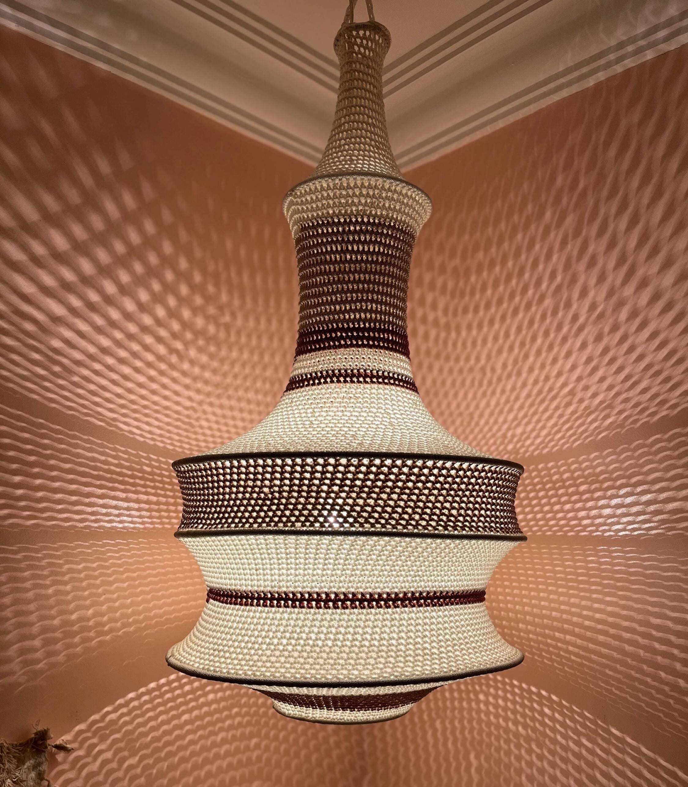 A pendant light fixture featuring a woven, crocheted-style shade with a tiered, bell-shaped silhouette. The design…