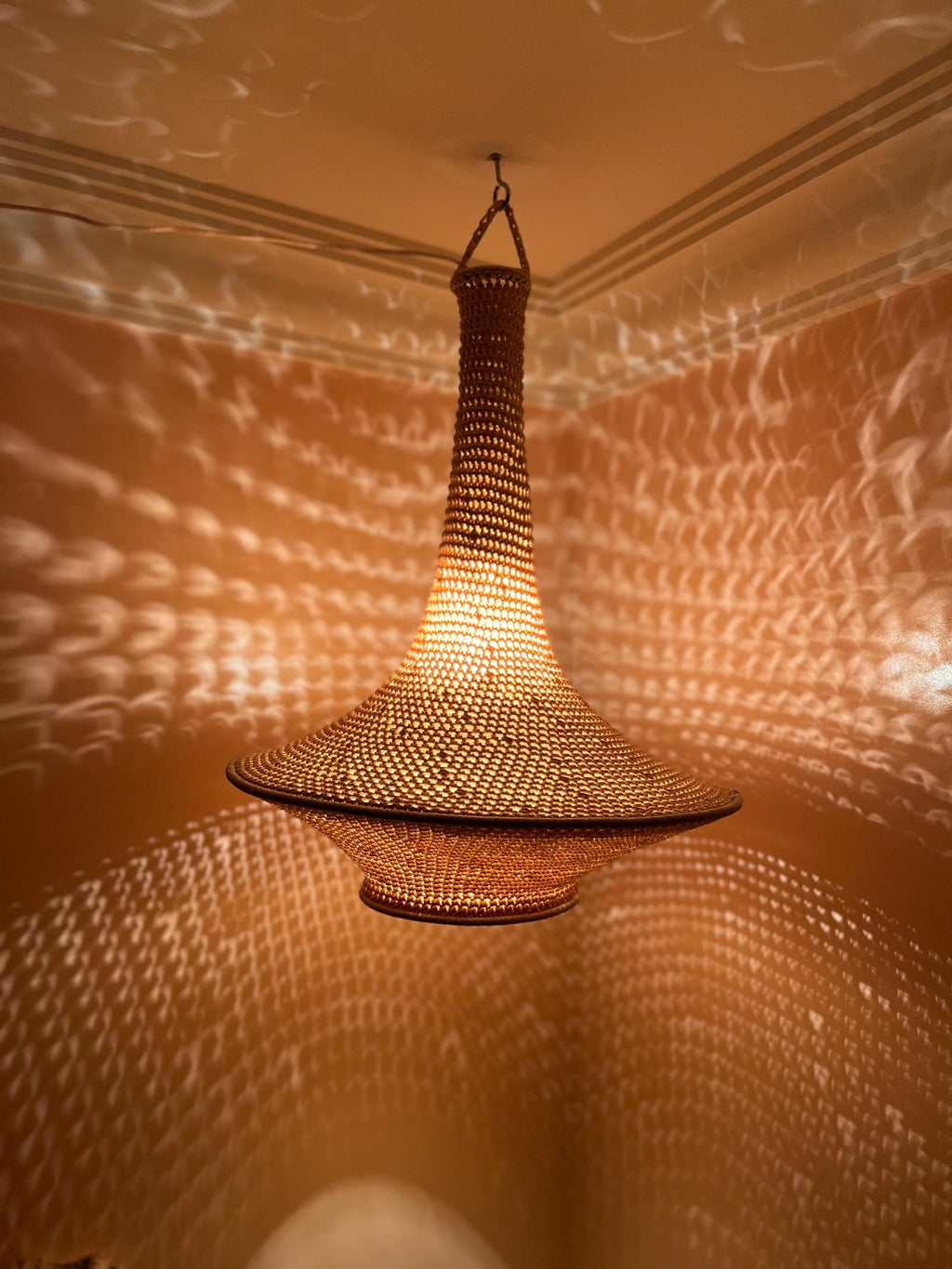 A hanging pendant light fixture featuring a woven, tan-colored material with a wide, flared base and a tall, narrow neck.…