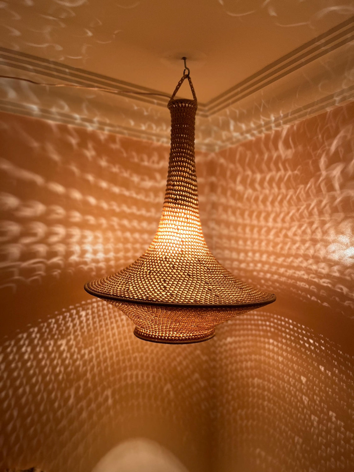 A hanging pendant light fixture featuring a woven, tan-colored material with a wide, flared base and a tall, narrow neck.…