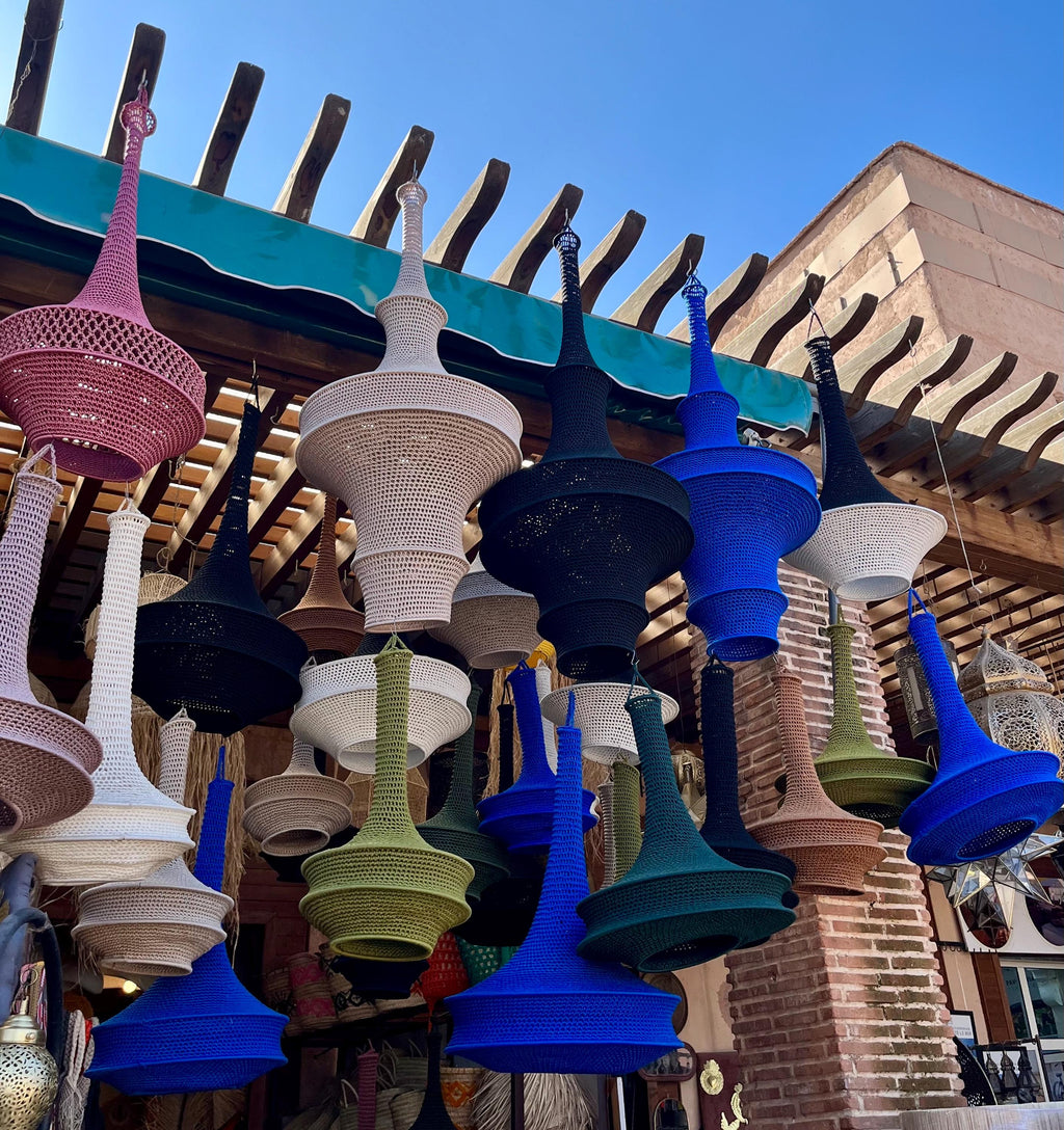 A collection of hanging pendant lamps featuring woven, bell-shaped shades in various colors including pink, white, black,…