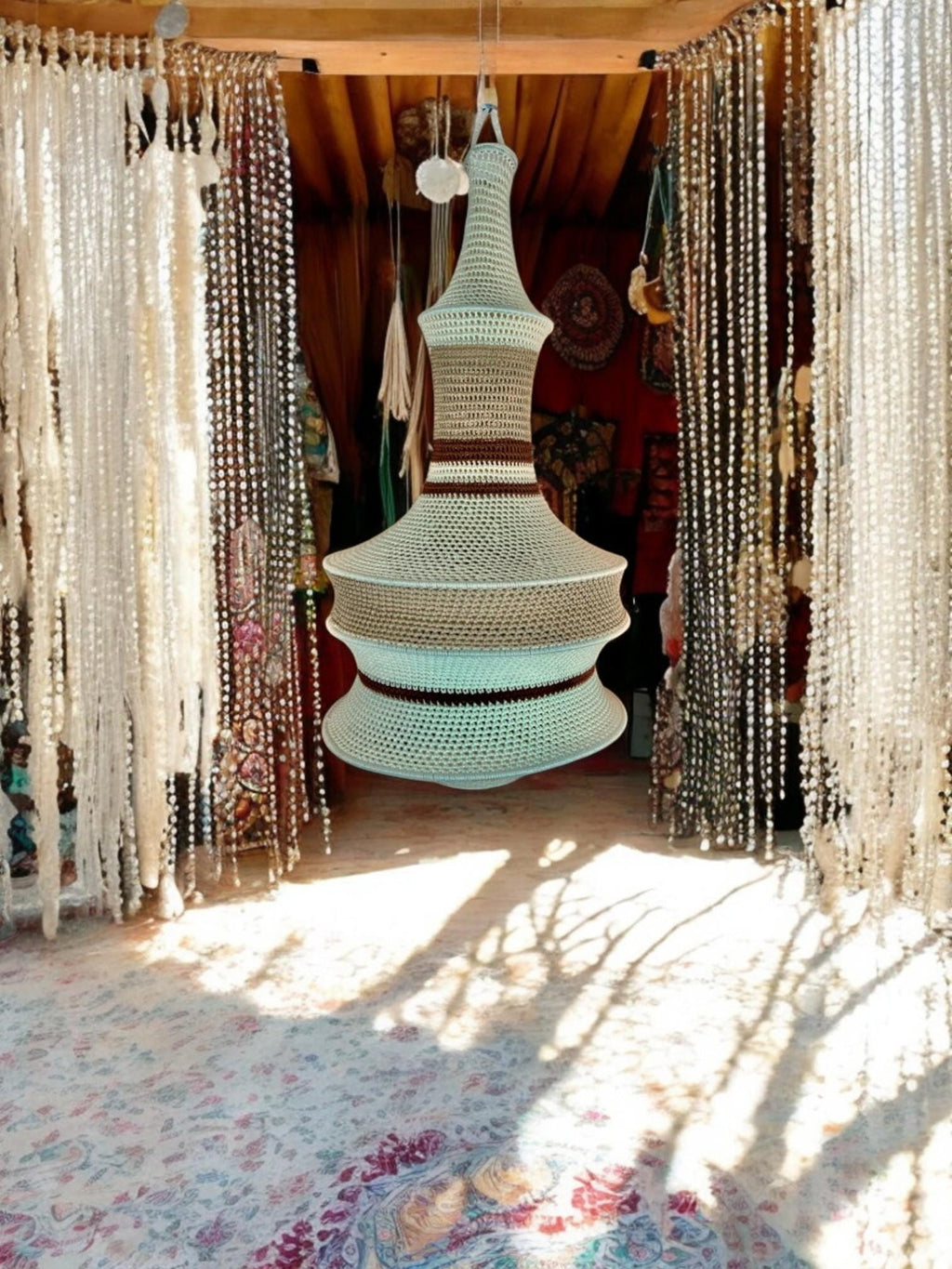 A hanging pendant light fixture featuring a crocheted shade in alternating horizontal bands of light mint green, beige,…
