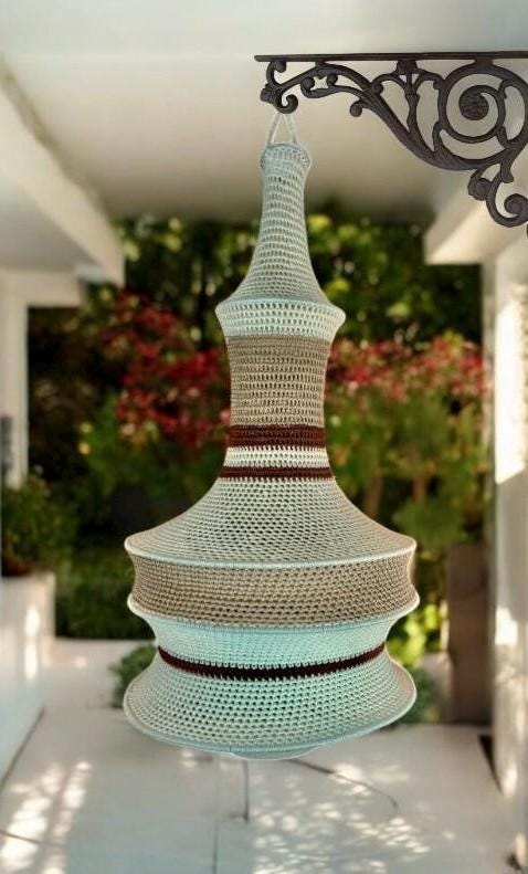 A hanging crochet lamp shade featuring a tiered, bell-shaped silhouette. The design incorporates horizontal stripes in…