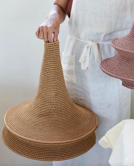 A tan, cone-shaped, crocheted lampshade with a wide, circular base and a narrow top opening. The texture is uniform and…
