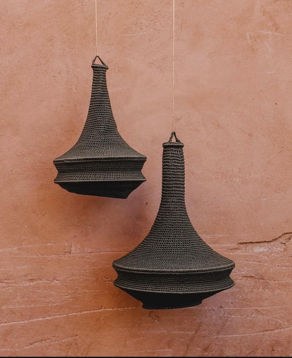 Two dark charcoal gray hanging pendant lamps featuring a textured, crocheted exterior. Each lamp has a narrow, elongated…