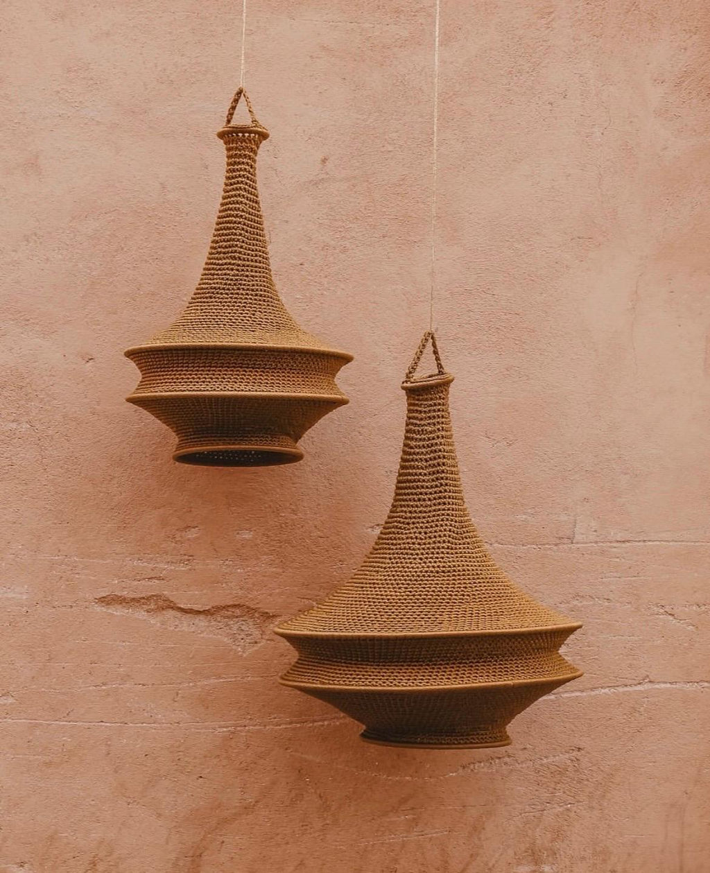 Two hanging pendant lamps crafted from brown crocheted fiber. Each lamp features a tall, tapered neck and a wide, tiered…