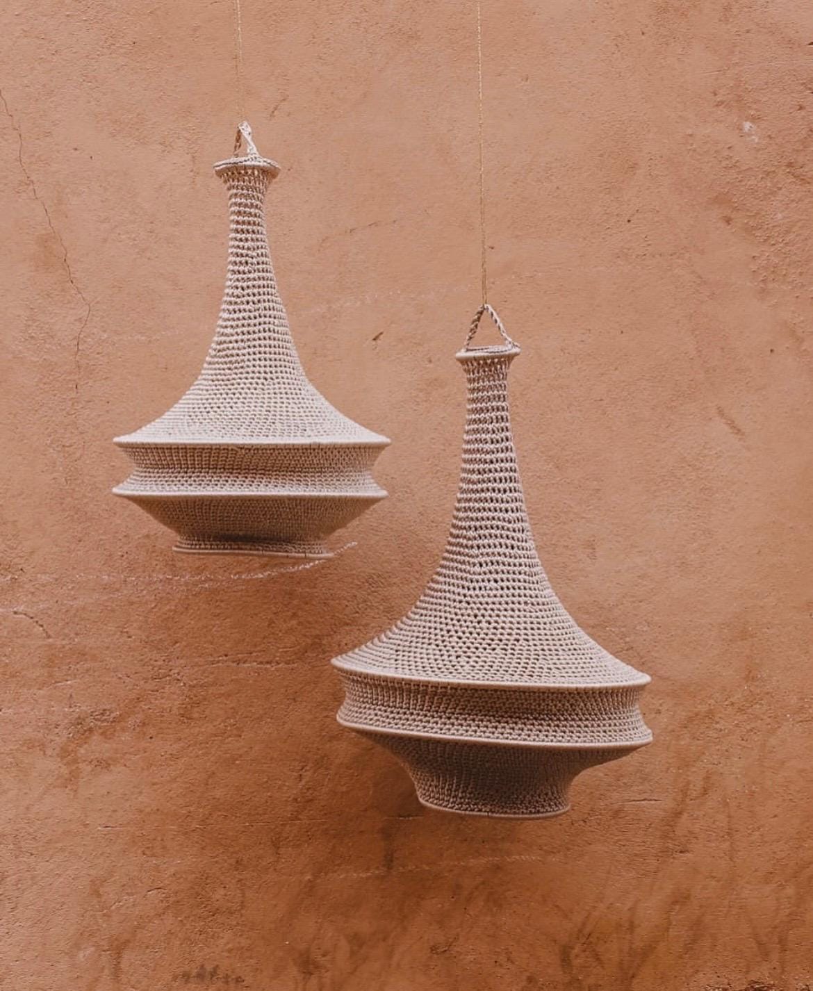 Two hanging pendant lamps featuring a beige crocheted exterior with a wide, rounded base that tapers into a long, narrow…