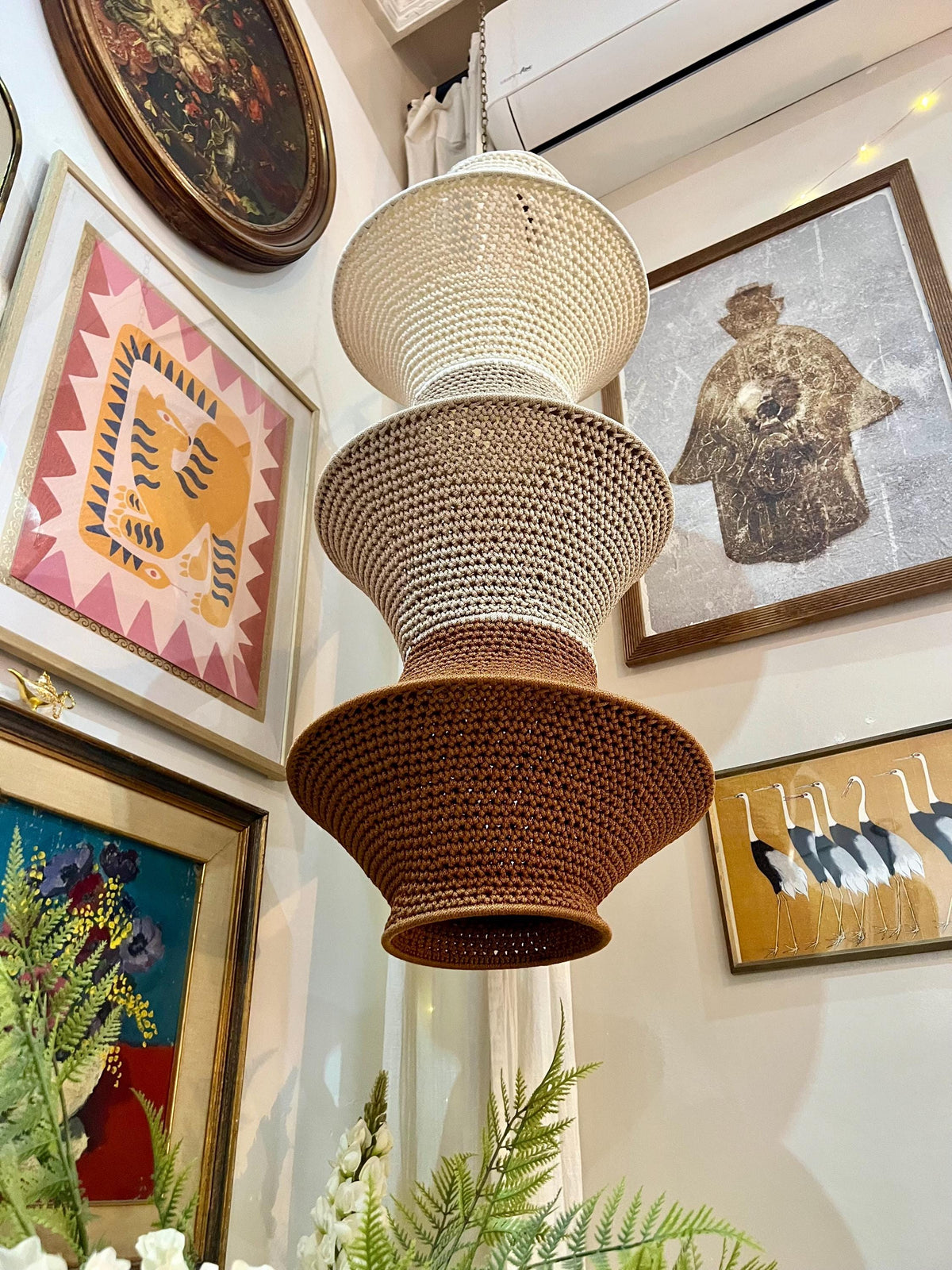 A hanging pendant light fixture featuring three stacked, flared, bowl-shaped shades made of crocheted fiber. The top…