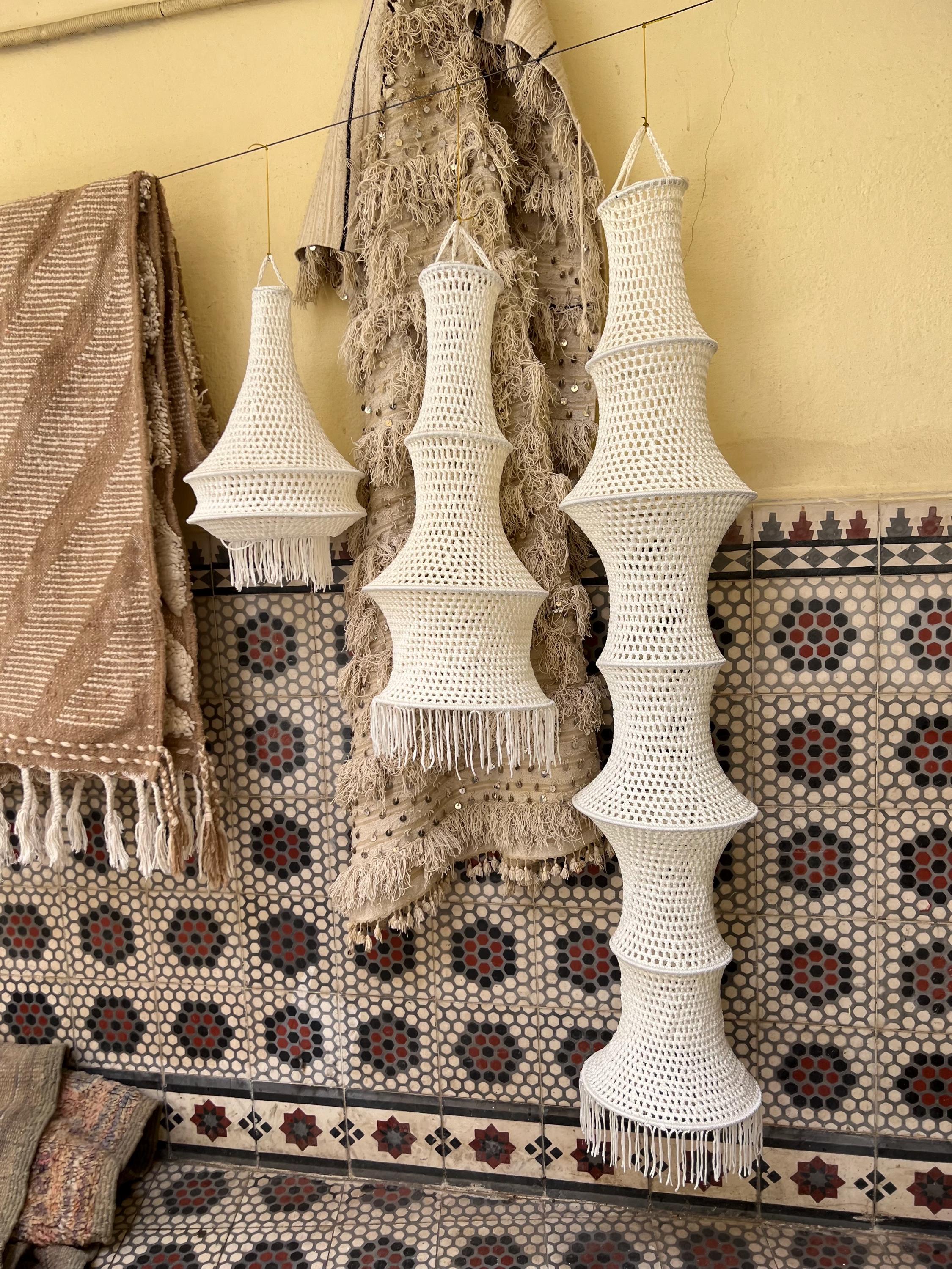 Three off-white crocheted hanging lampshades of varying heights and tiered shapes. Each shade features a fine mesh…