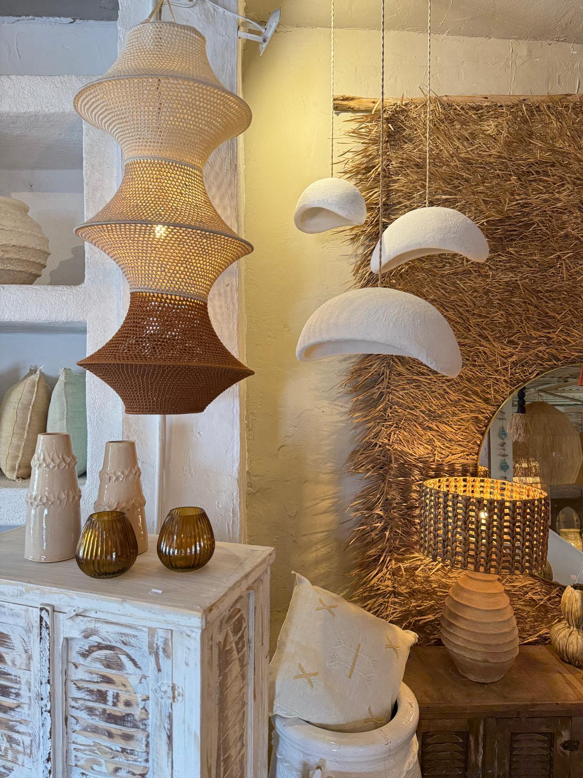 A large, three-tiered pendant light with a woven texture, transitioning from cream to tan to brown. Nearby, three white,…