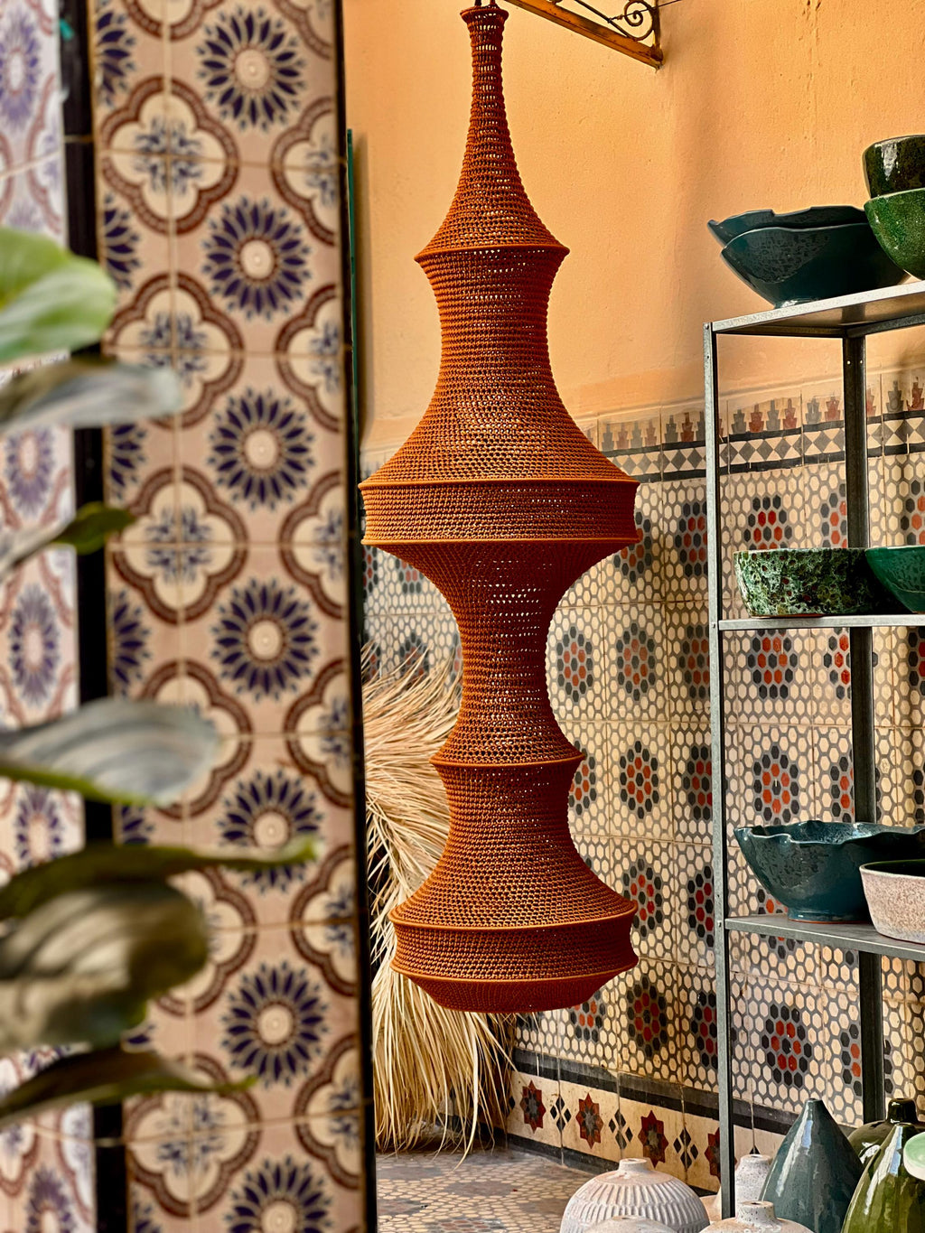 A tall, hanging pendant light fixture featuring a vibrant orange, intricately crocheted or woven texture. The structure…