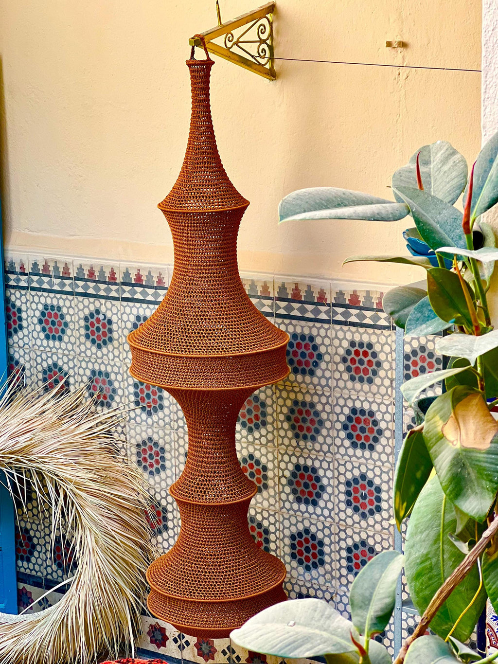 A tall, rust-colored, cylindrical pendant light fixture with a complex, woven, open-mesh texture. The structure features…