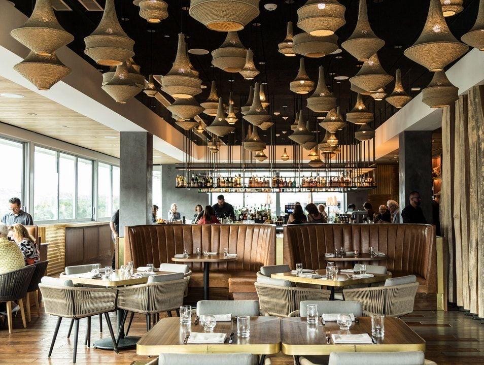 A restaurant interior featuring numerous beige woven pendant lights suspended from a dark ceiling. The space includes…