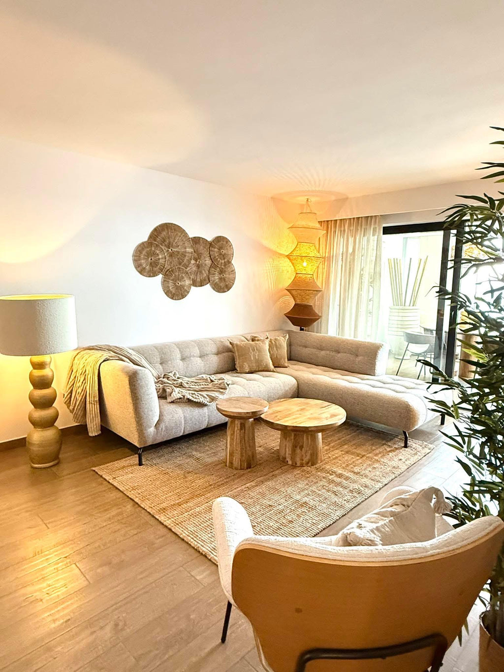 A light gray sectional sofa with a chaise, two round wooden side tables, a textured jute rug, a floor lamp with a gold…