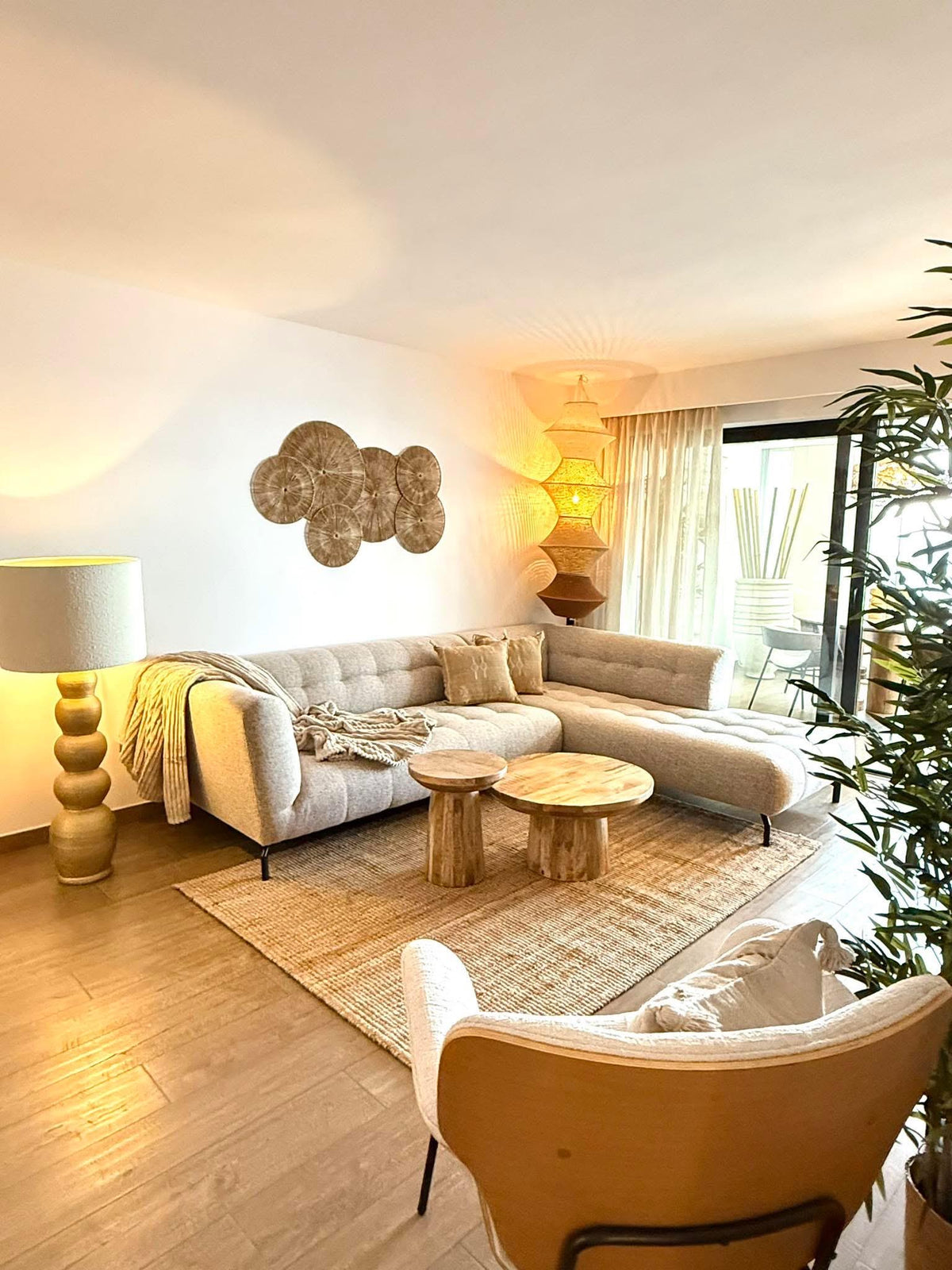 A light gray sectional sofa with a chaise, two round wooden side tables, a textured jute rug, a floor lamp with a gold…