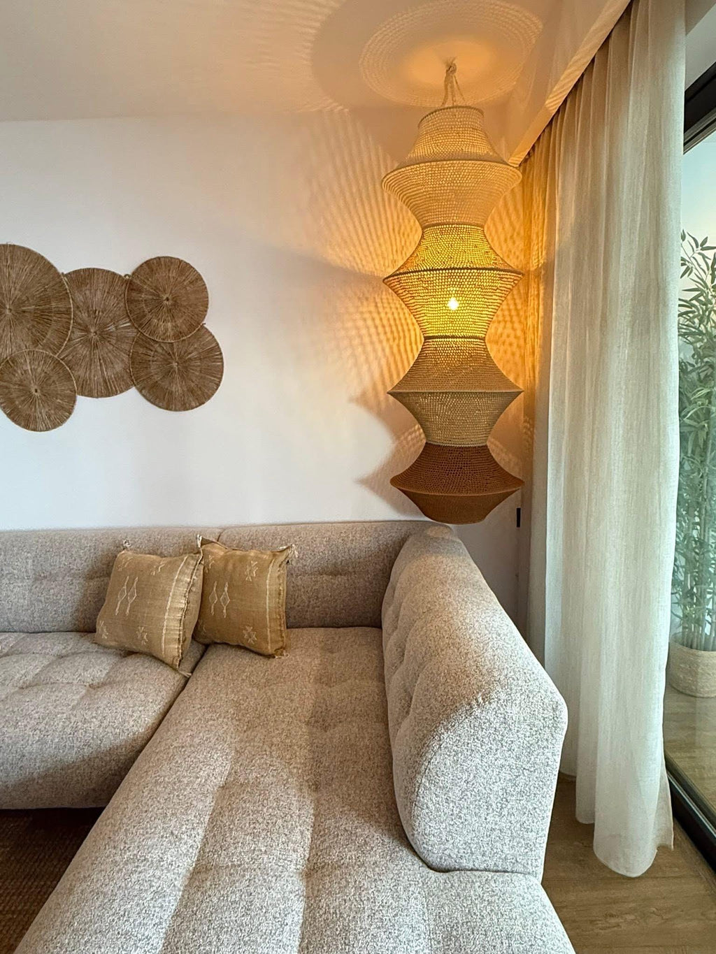 A tall, multi-tiered hanging pendant lamp made of woven natural fiber, featuring a gradient of beige to brown tones. The…