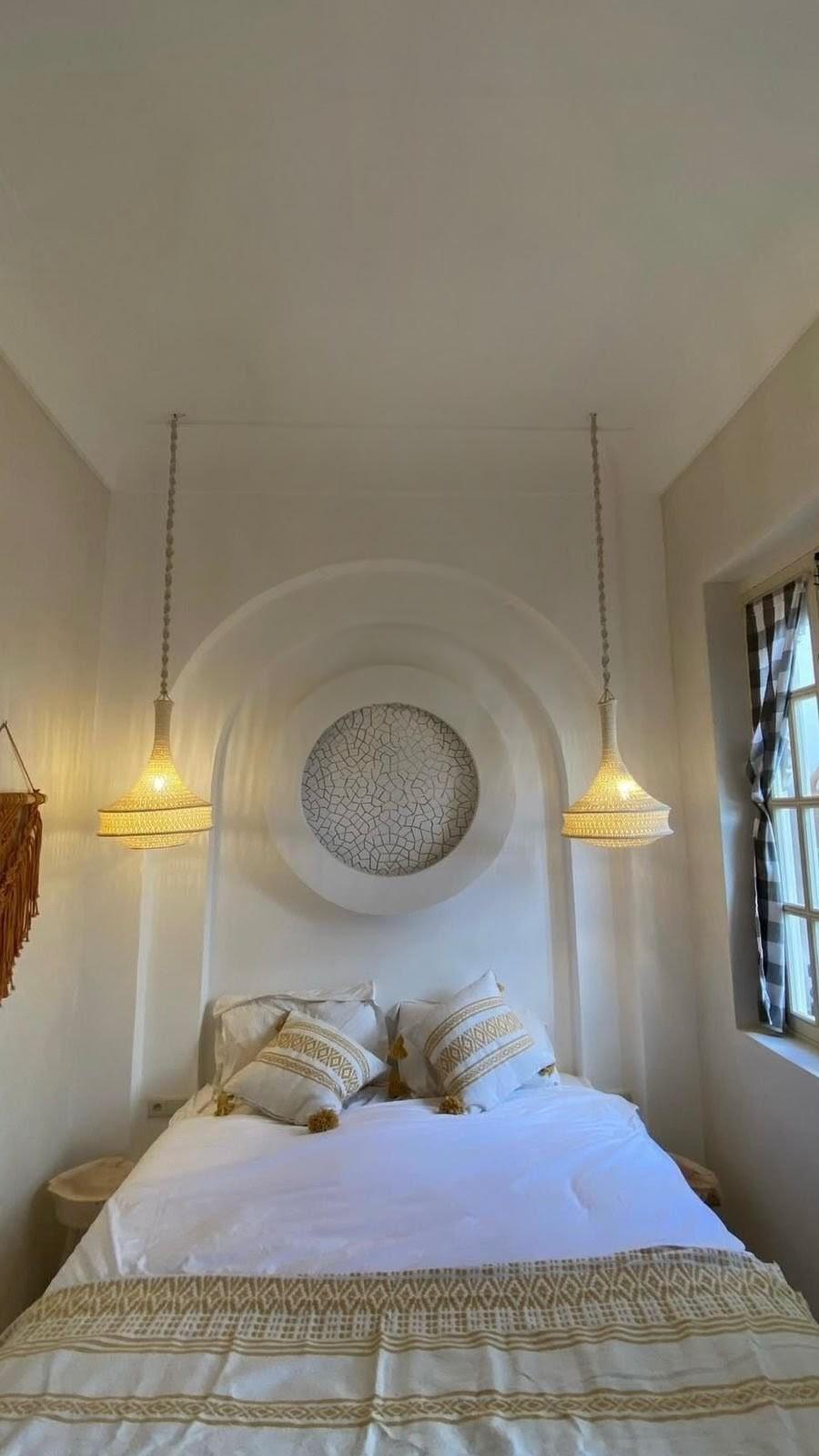A bedroom featuring a white bed with a patterned throw blanket and two matching pillows with tassels. Two woven pendant…