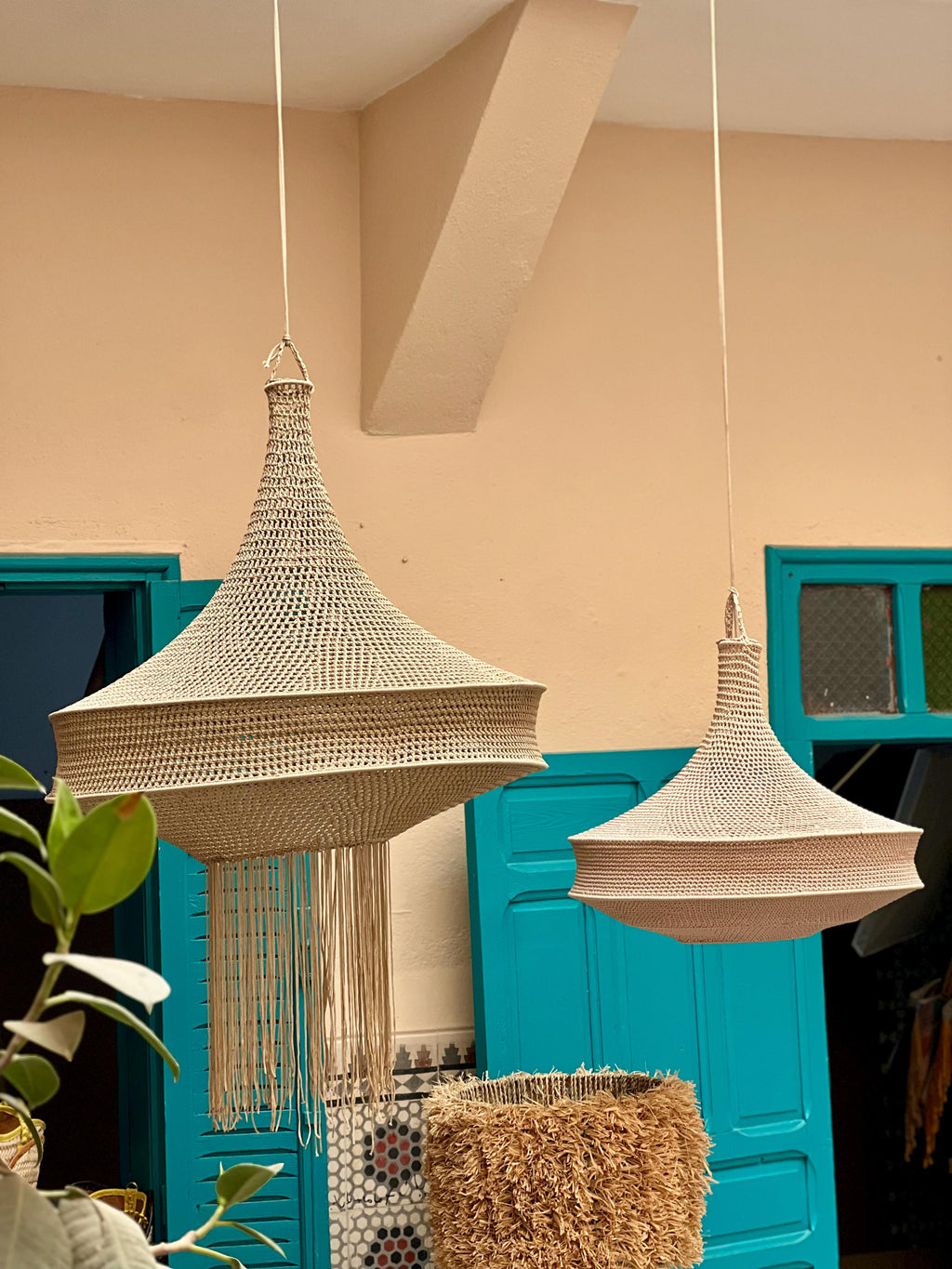 Two beige pendant lamps with a woven, bell-shaped structure suspended from the ceiling. The larger lamp on the left…