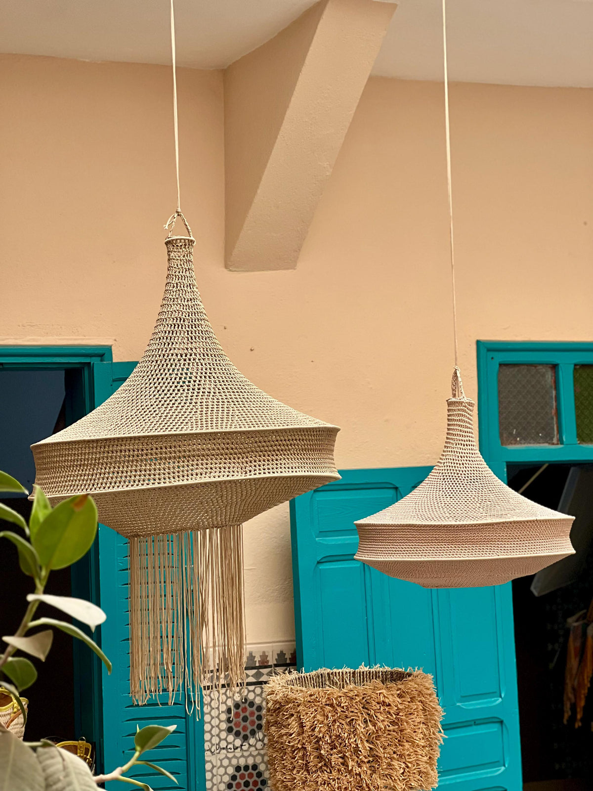 Two beige pendant lamps with a woven, bell-shaped structure suspended from the ceiling. The larger lamp on the left…
