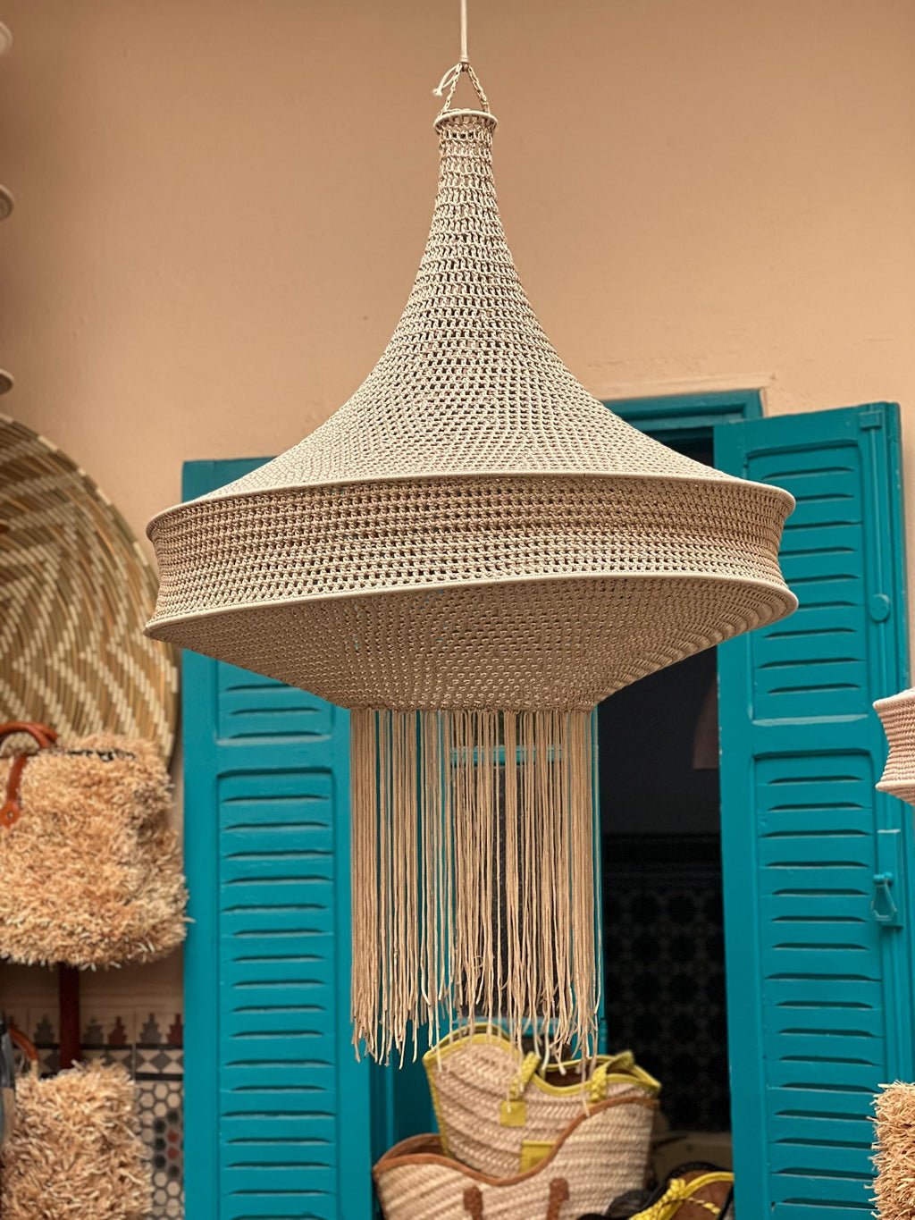 A beige, bell-shaped pendant light fixture crafted from tightly woven cord. The structure features a wide, tiered…