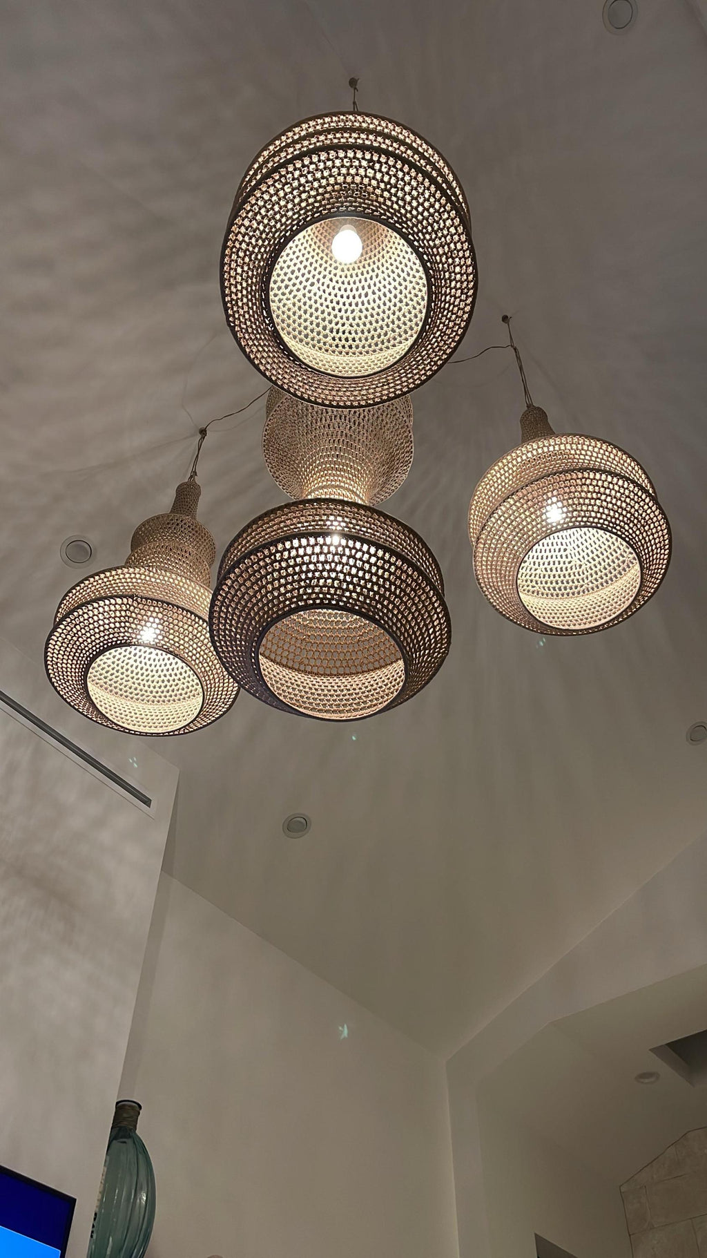 A cluster of four pendant lights featuring woven tan rattan shades with a circular, tiered design. Each shade has an…