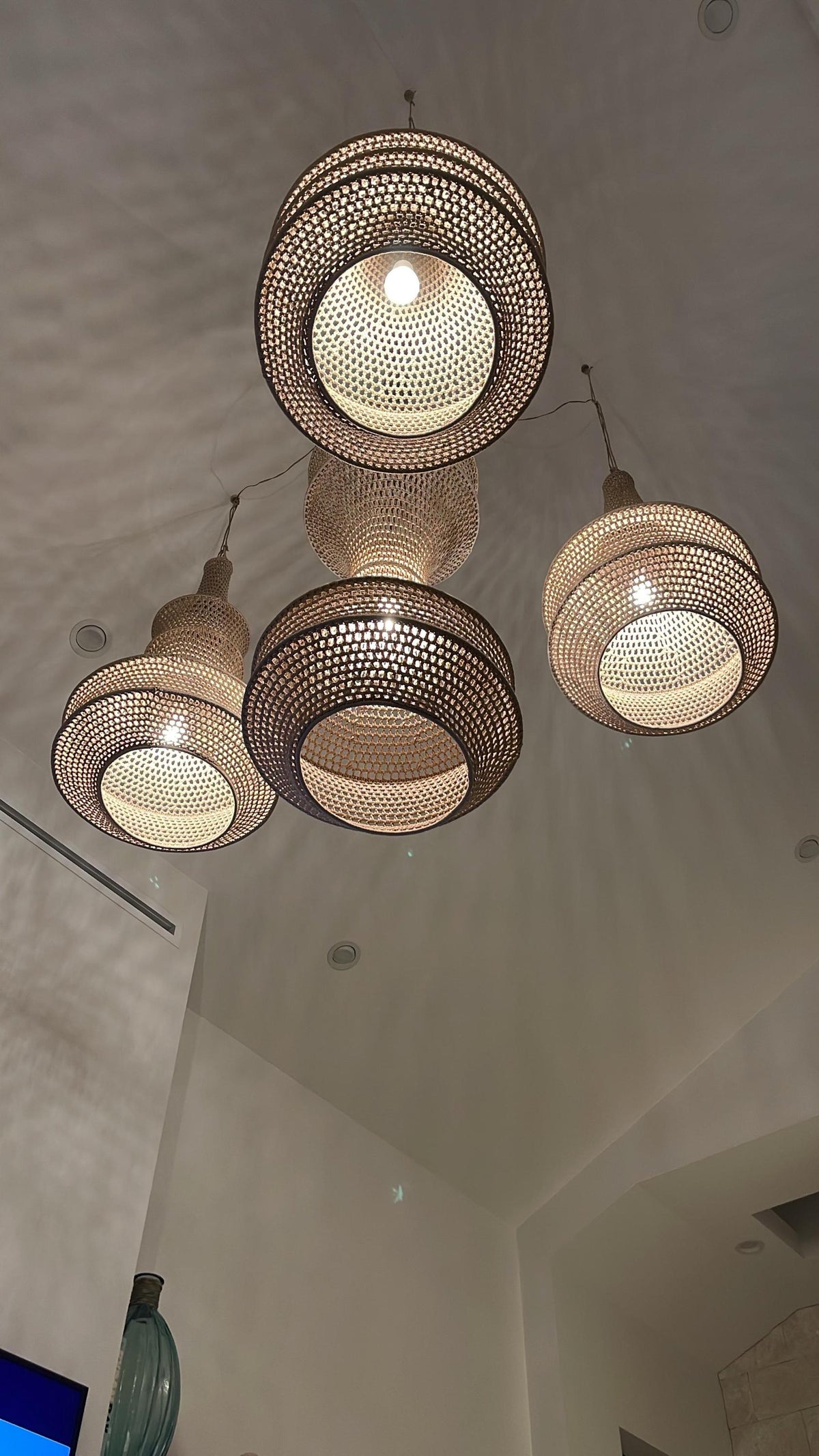 A cluster of four pendant lights featuring woven tan rattan shades with a circular, tiered design. Each shade has an…
