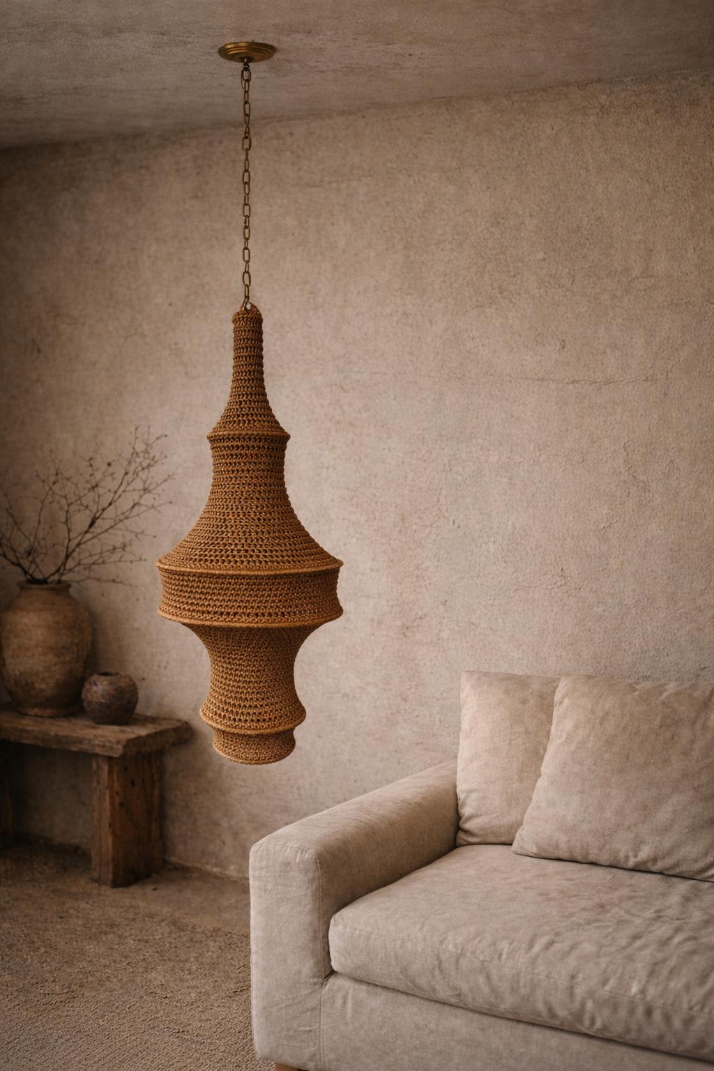 A large, bell-shaped pendant light fixture featuring a textured, tan-colored crocheted or woven exterior. The lamp is…
