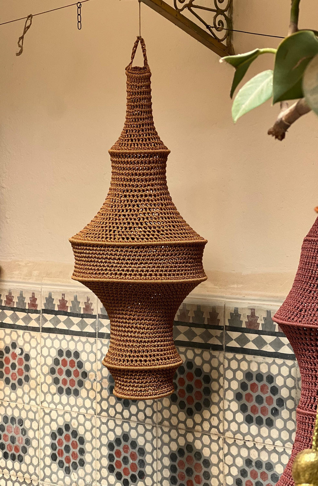 A hanging pendant light shade crafted from brown yarn in a crochet technique. The shade features a multi-tiered,…