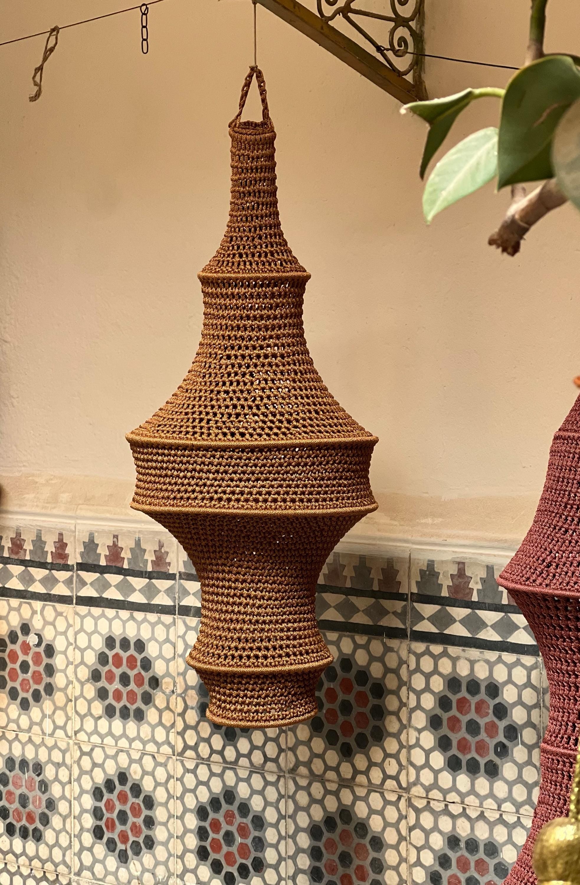 A hanging pendant light shade crafted from brown yarn in a crochet technique. The shade features a multi-tiered,…