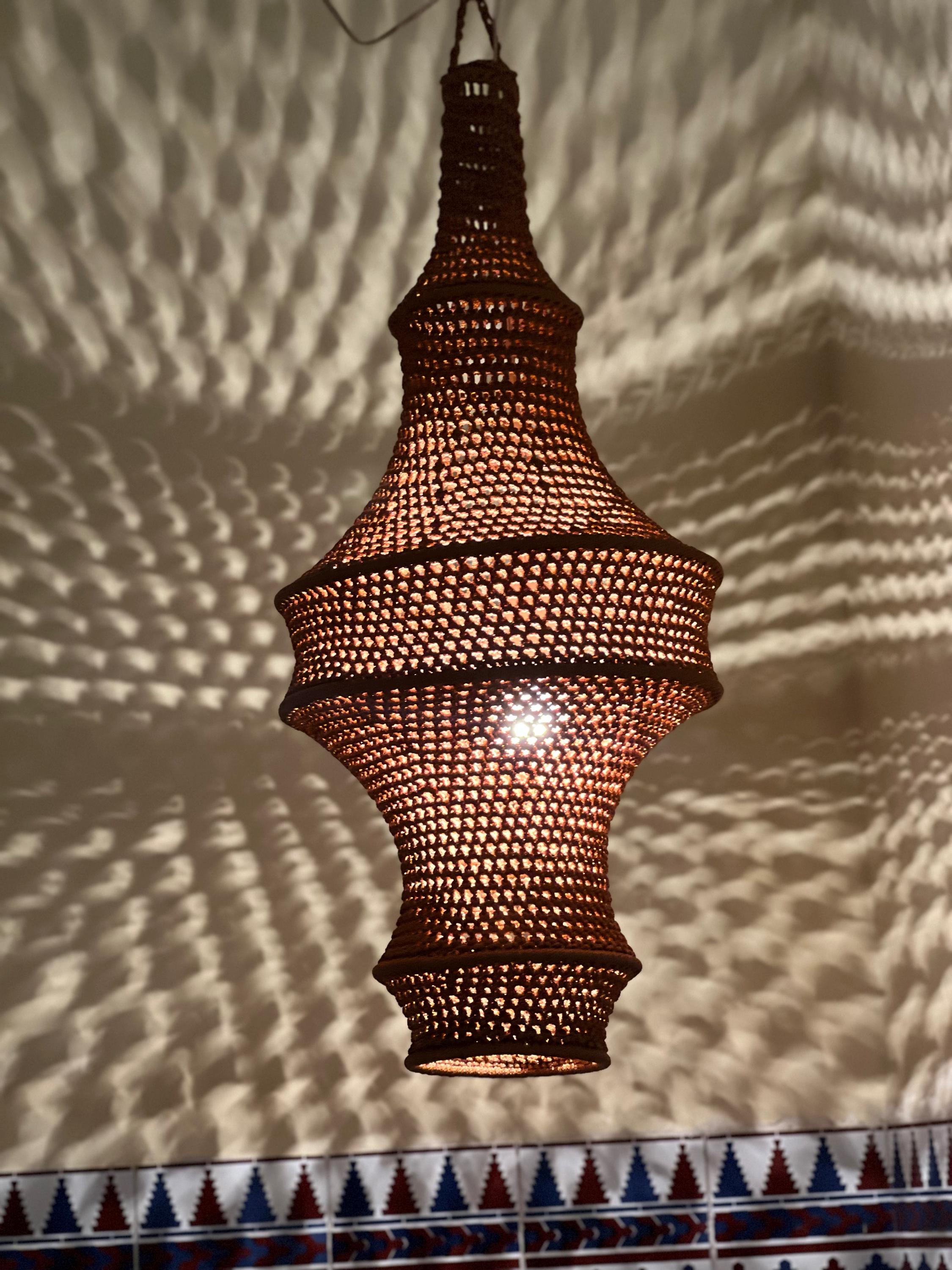 A hanging pendant light fixture featuring a brown, intricately crocheted or woven mesh shade with a bulbous, multi-tiered…