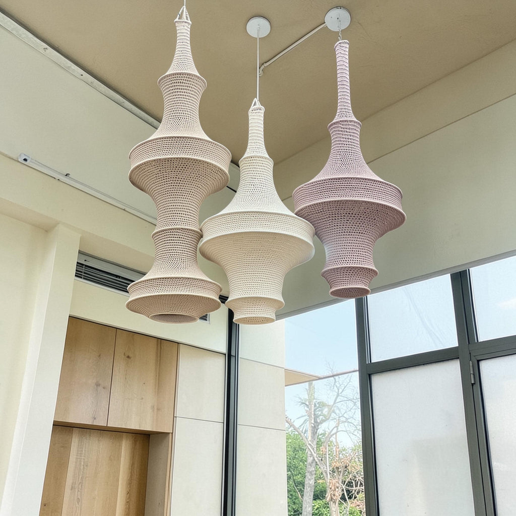 Three hanging pendant lights featuring intricate crochet textures. The left light is a tall beige shade, the center is a…