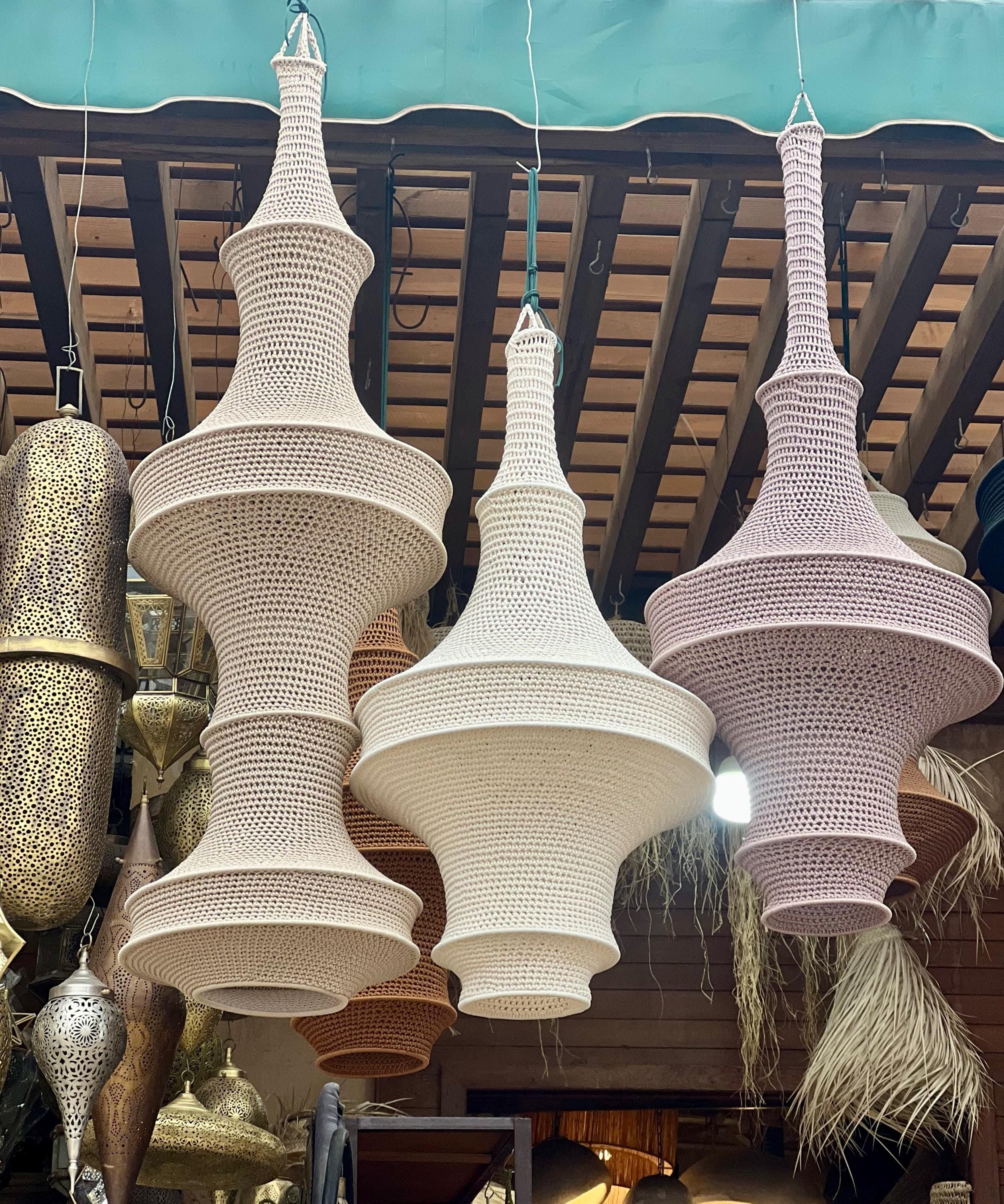 Three hanging pendant lamps featuring intricate crochet work in shades of cream, off-white, and light pink. Each lamp has…