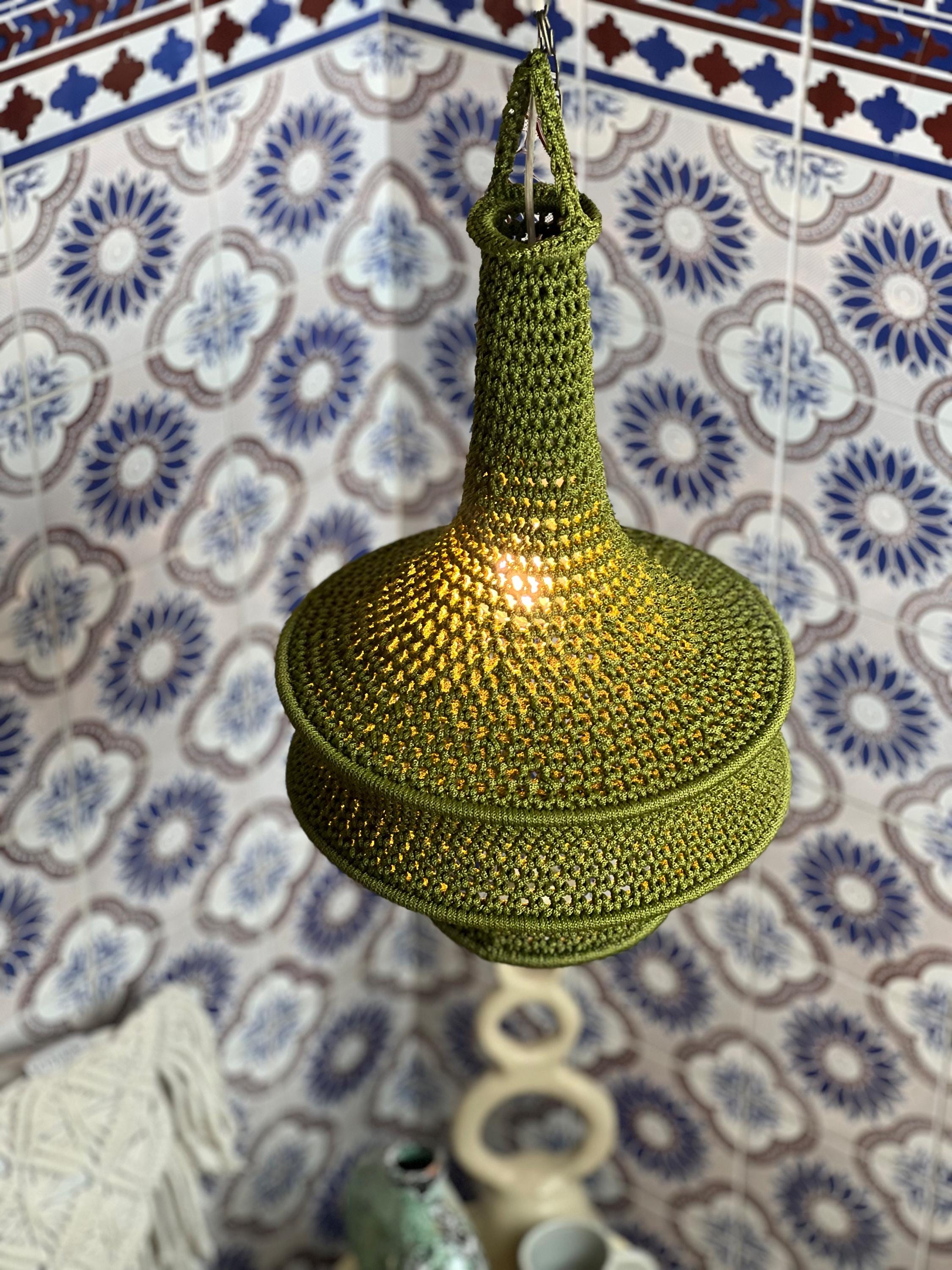 A hanging pendant lamp featuring a textured, olive green crocheted shade with a tapered neck and a wide, rounded base.…