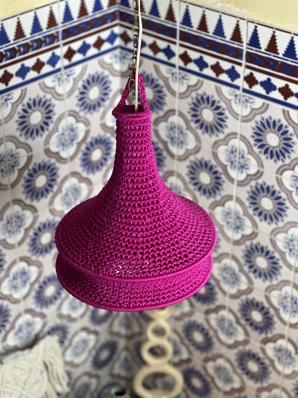 A vibrant magenta crochet lampshade featuring a bell-shaped silhouette with a textured, knotted yarn construction. The…