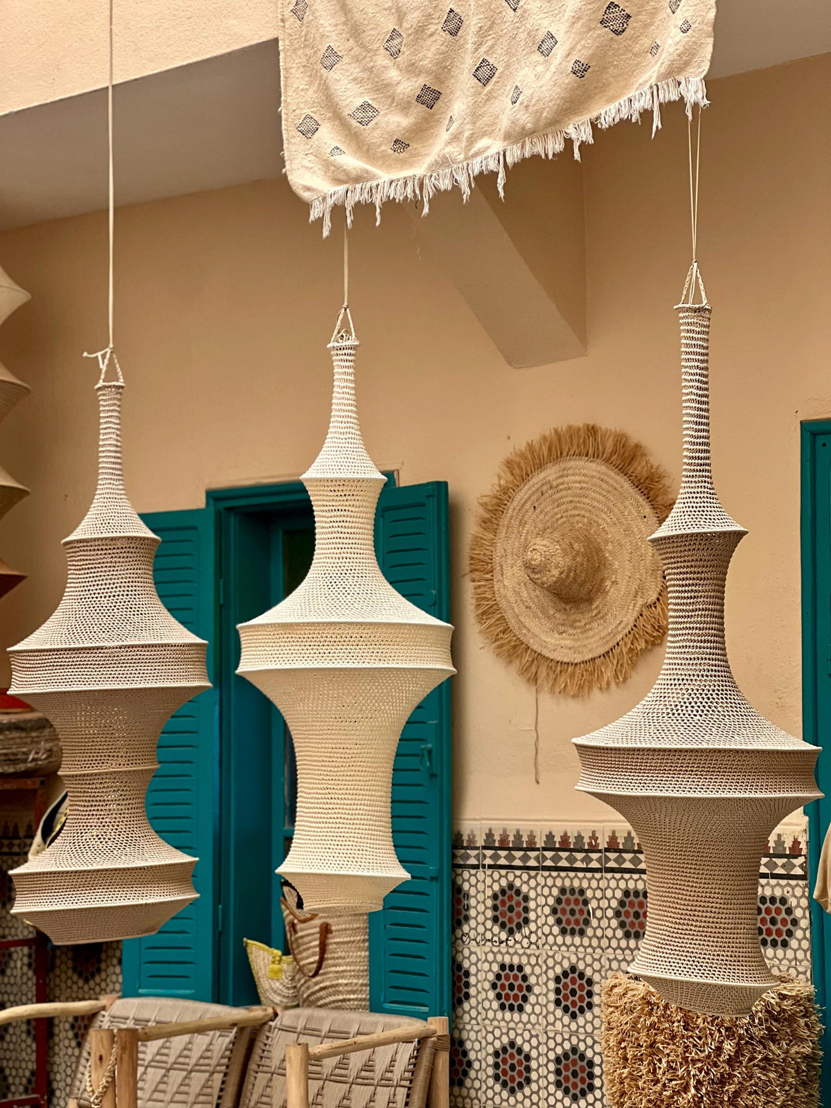 Three off-white, hand-crocheted pendant lamps hang vertically. Each lamp features a complex, multi-tiered hourglass shape…