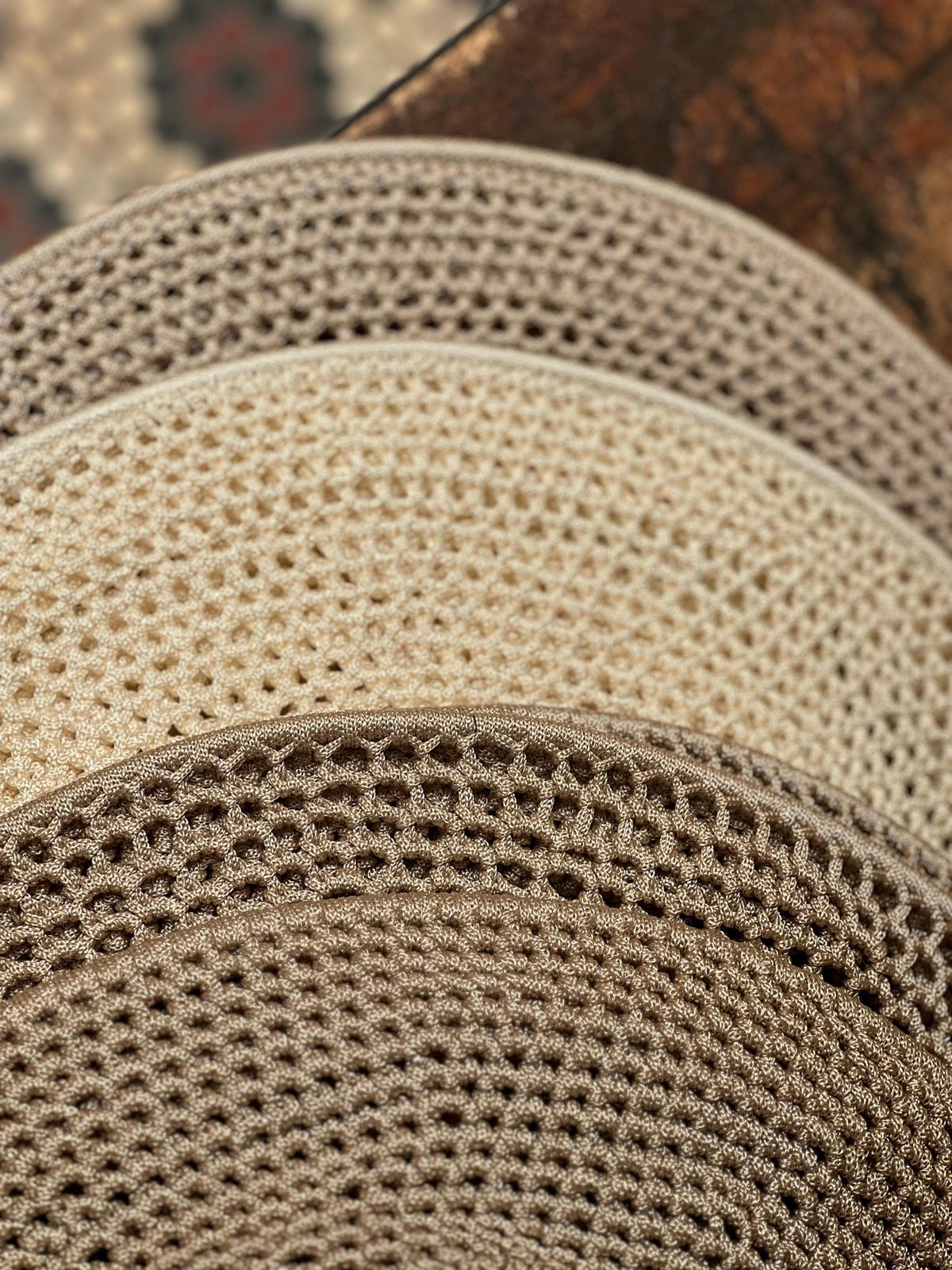 A stack of circular, crocheted mats featuring a consistent, open-weave mesh pattern. The mats are arranged in a gradient…