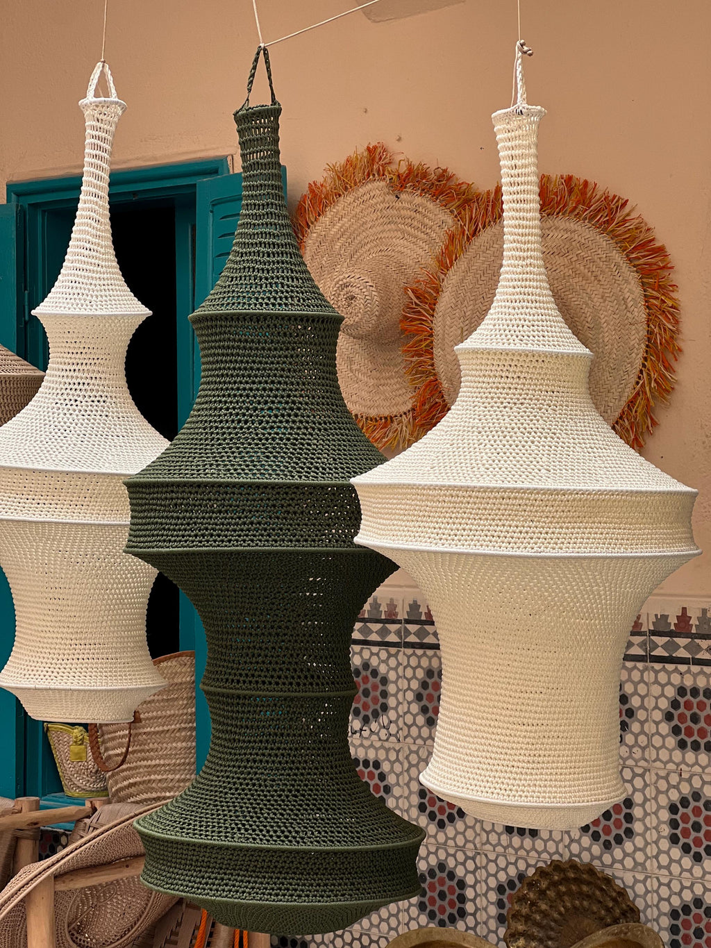 Three hanging pendant lamps featuring a crocheted textile construction. Two lamps are off-white and one central lamp is…