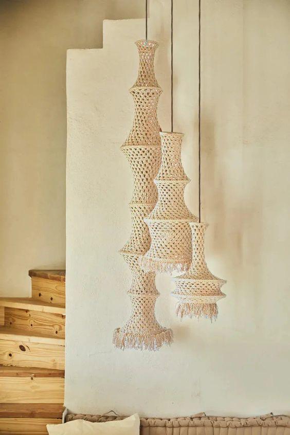 A cluster of beige macrame pendant lights of varying sizes hang from the ceiling. The lamps have a bell-like shape with a…